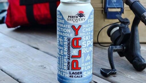 A non-alcoholic beer sitting on a wooden dock with fishing gear in the background.