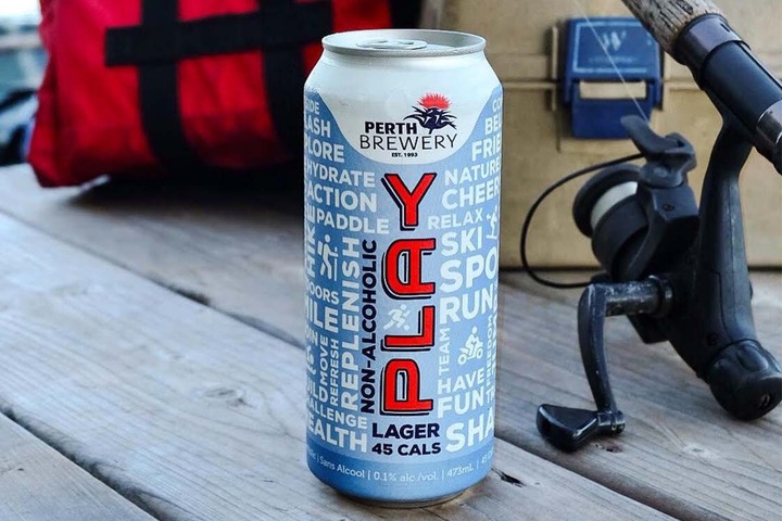 A non-alcoholic beer sitting on a wooden dock with fishing gear in the background.