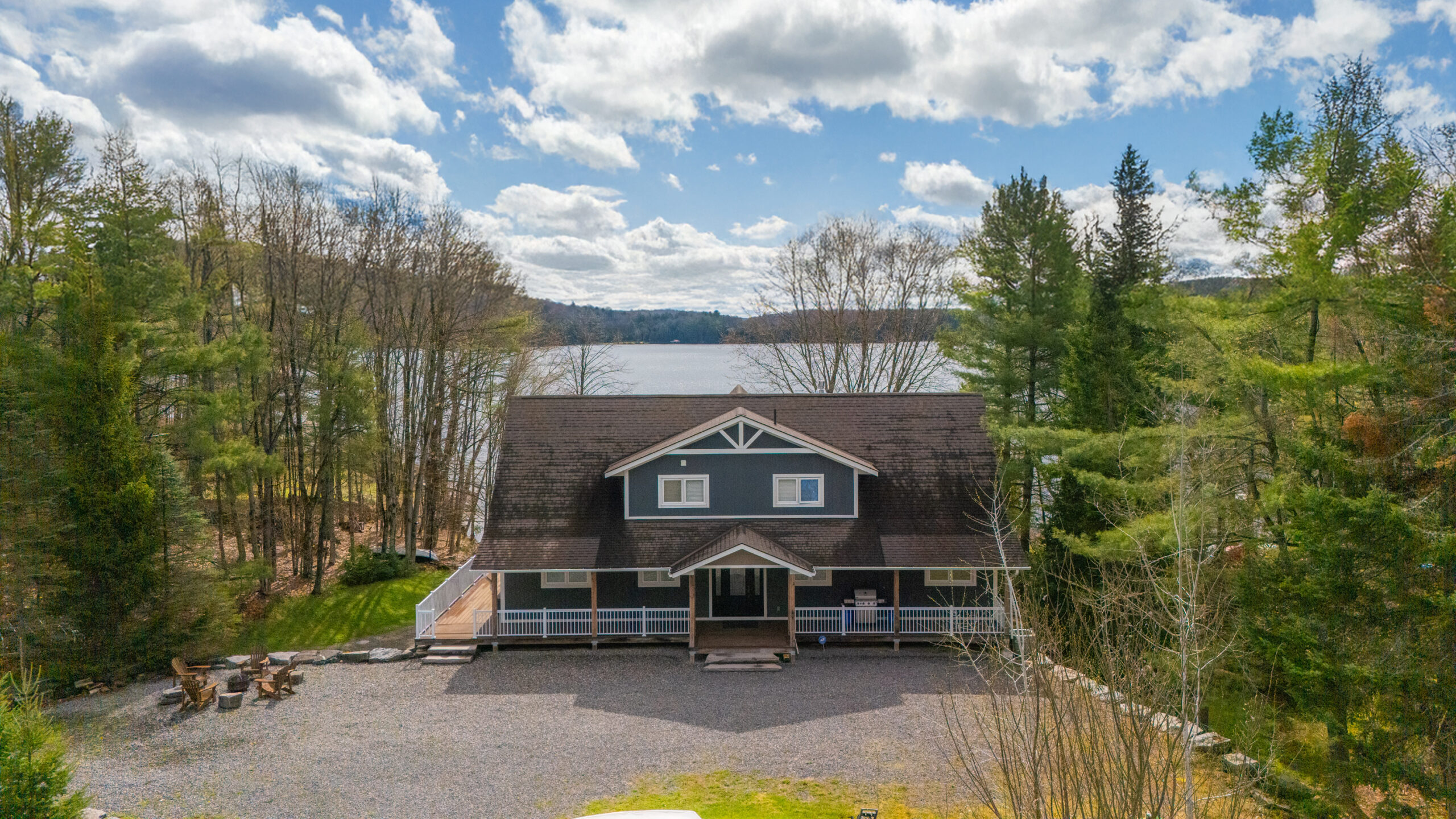 Cottage with a gravel driveway and fire pit, surrounded by trees