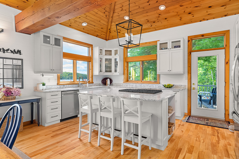Spacious kitchen with central island, white cabinetry, and wood-panelled ceilings in the main cottage