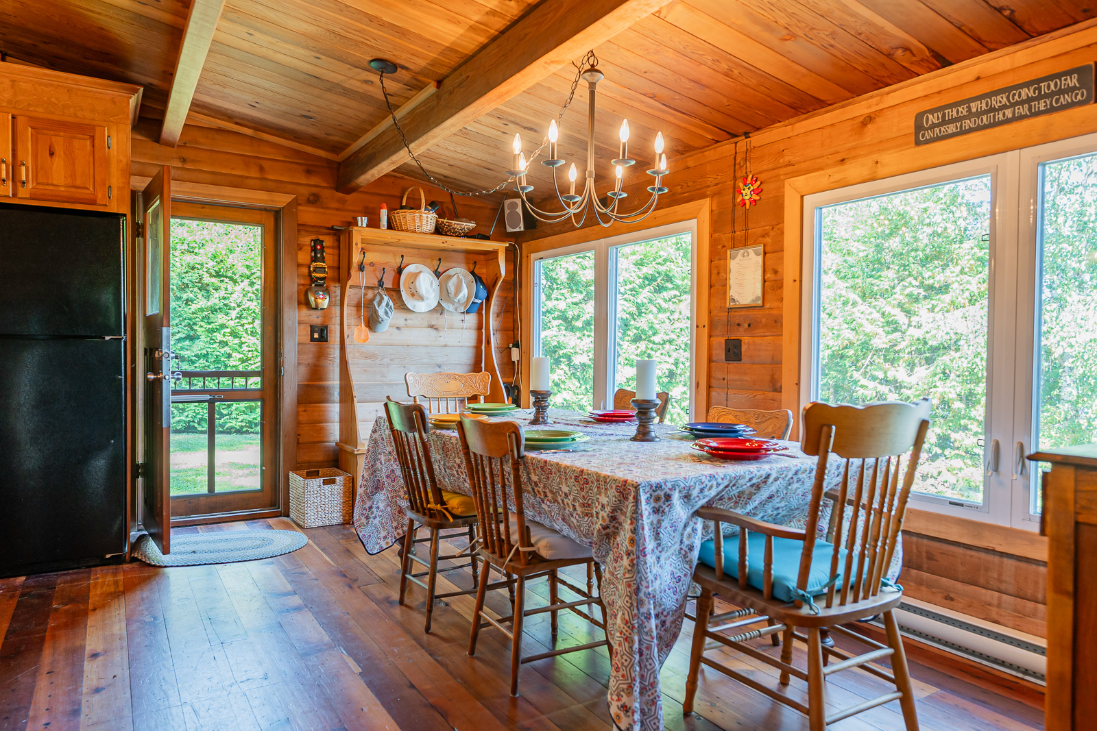 A dining table covered in a patterned tablecloth with bright windows facing the lake