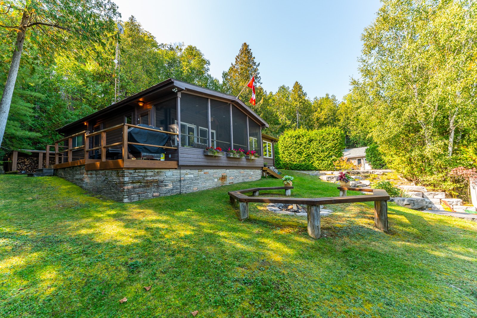A dark brown paneled cottage overlooks a rounded bench on a grassy yard