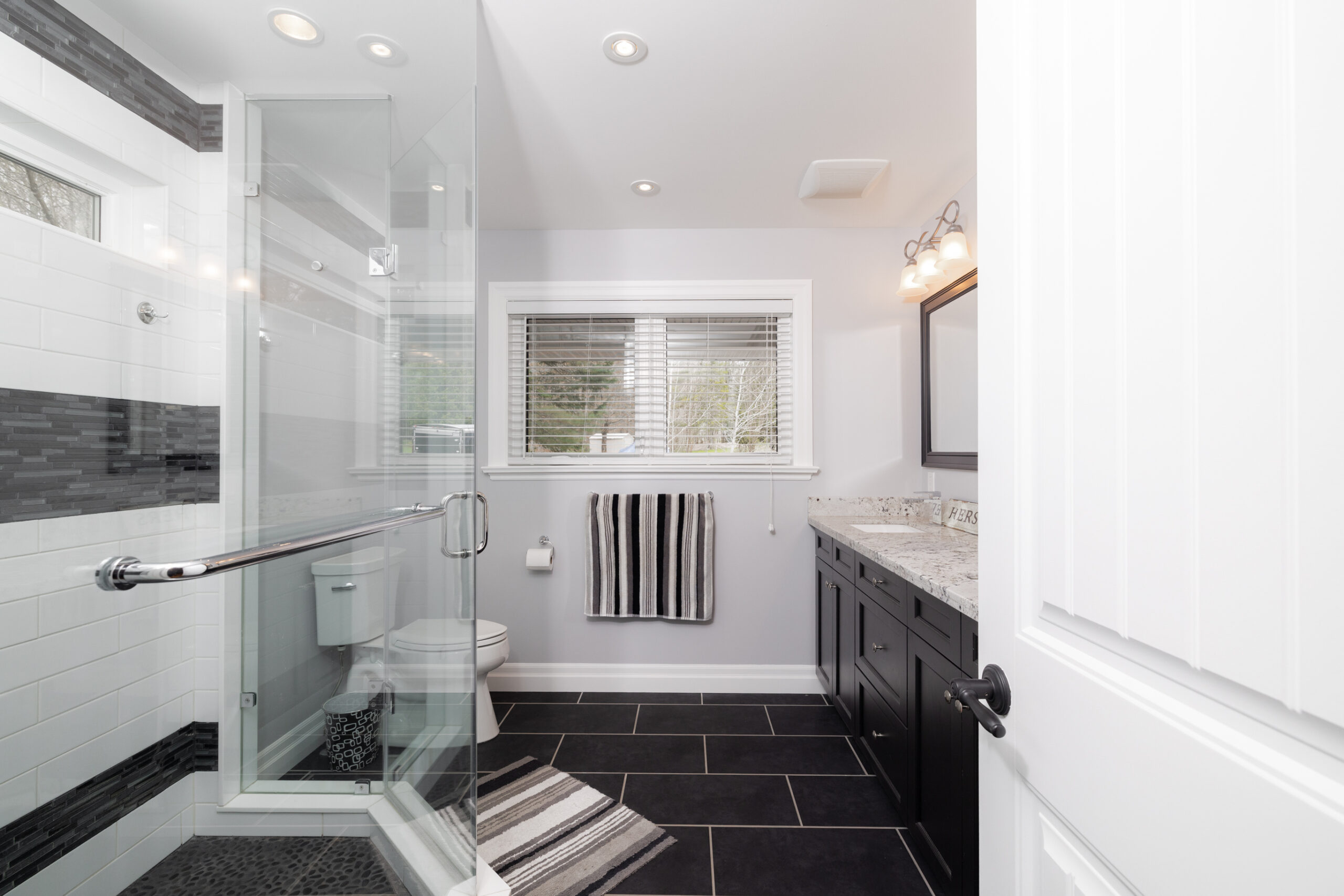 Bathroom with a glass shower, toilet, vanity, and window.