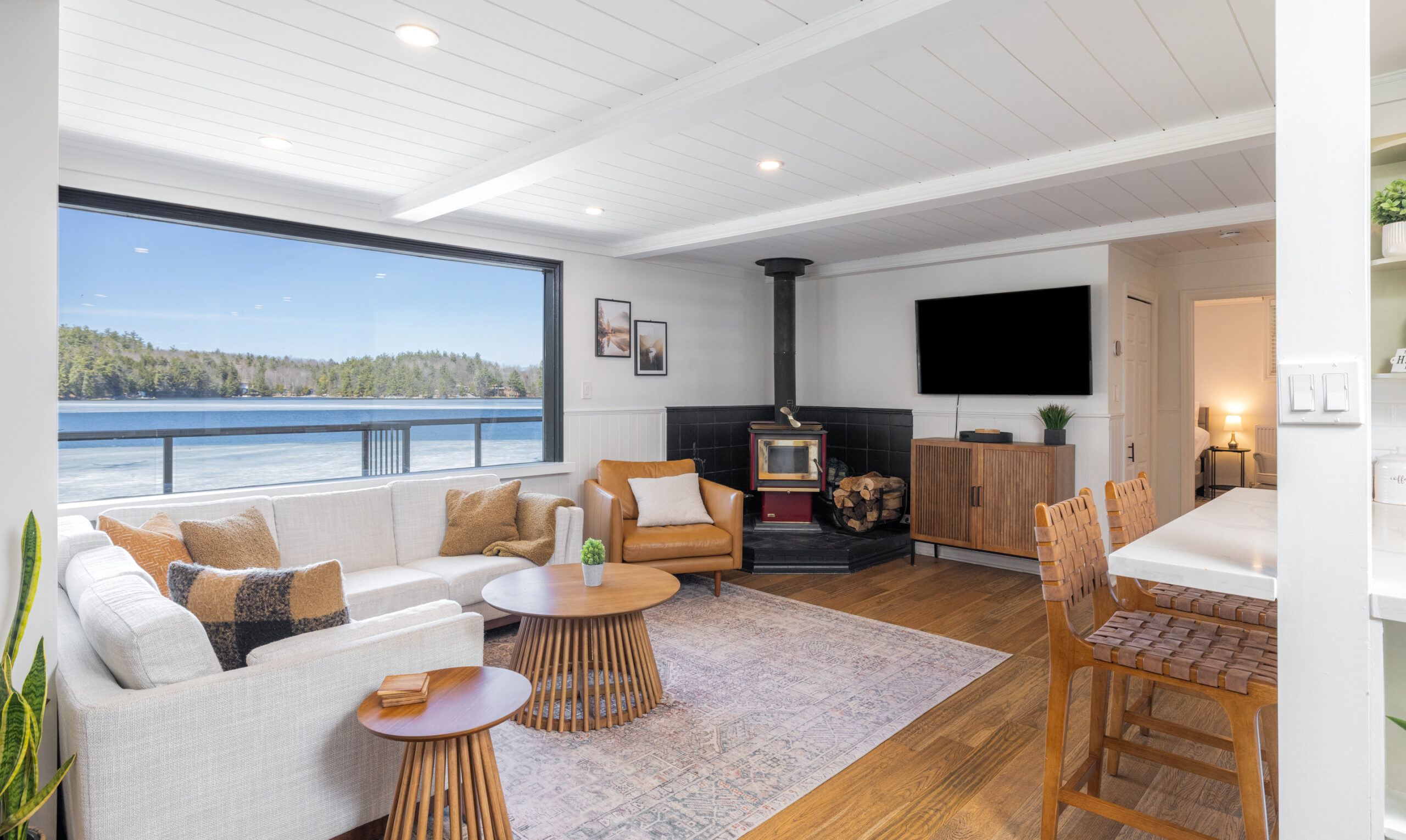 A white couch next to a bright lake-facing window faces a wood stove