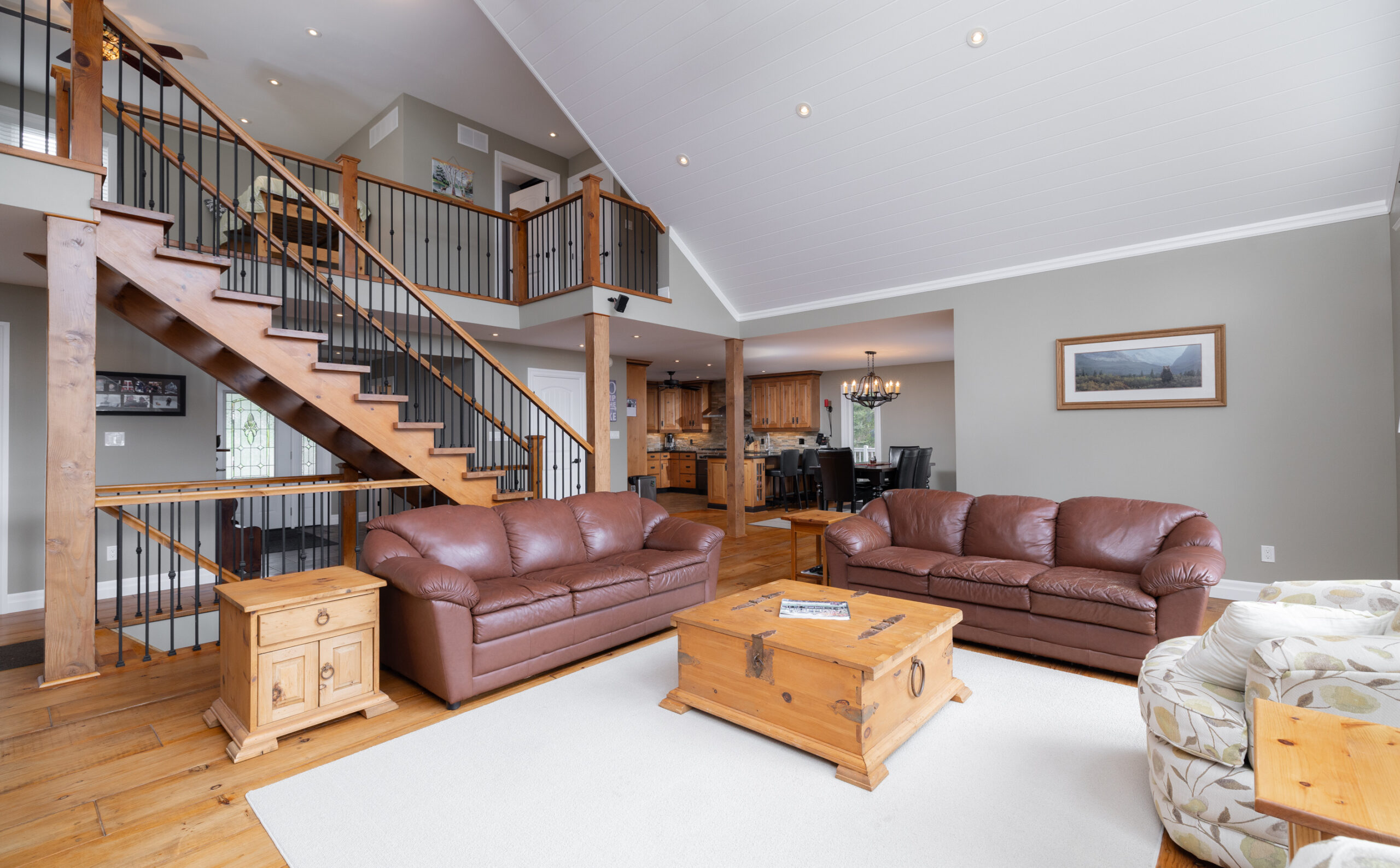 Open concept living room with brown couches, a coffee table, and wood stairs.
