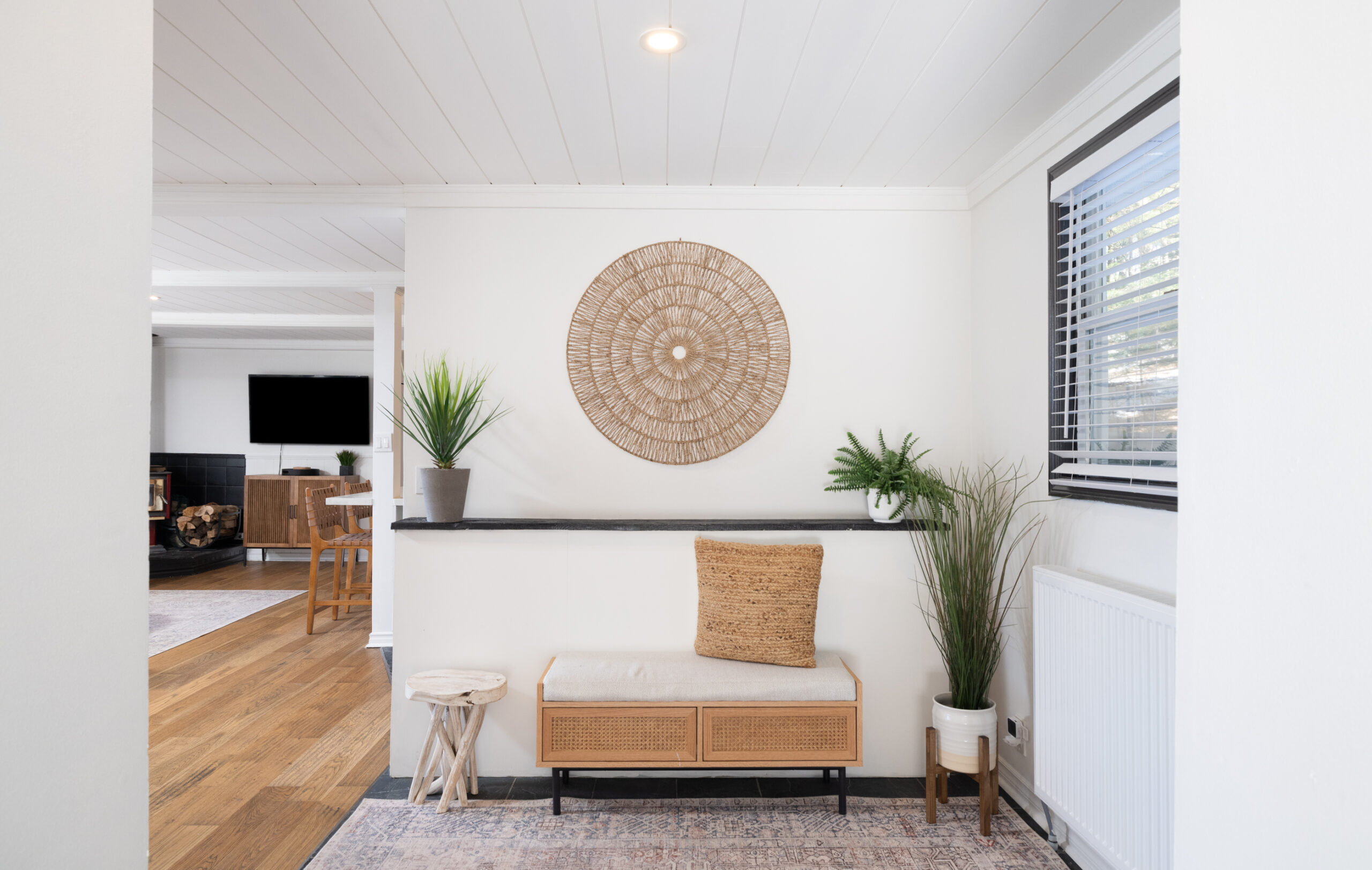 A white entryway with a small wood bench and patterned rug