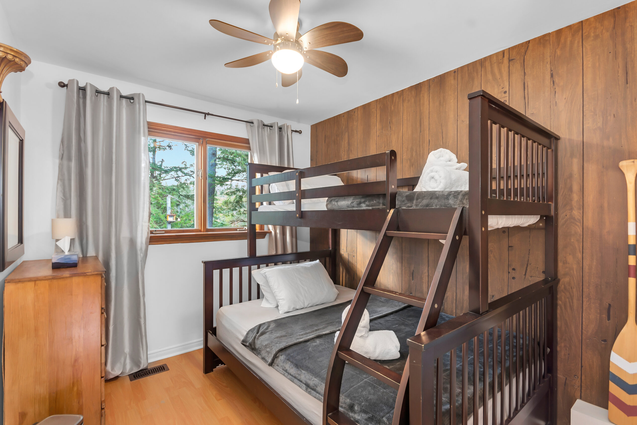 Dark wood bunkbeds in a white bedroom with a wood wall