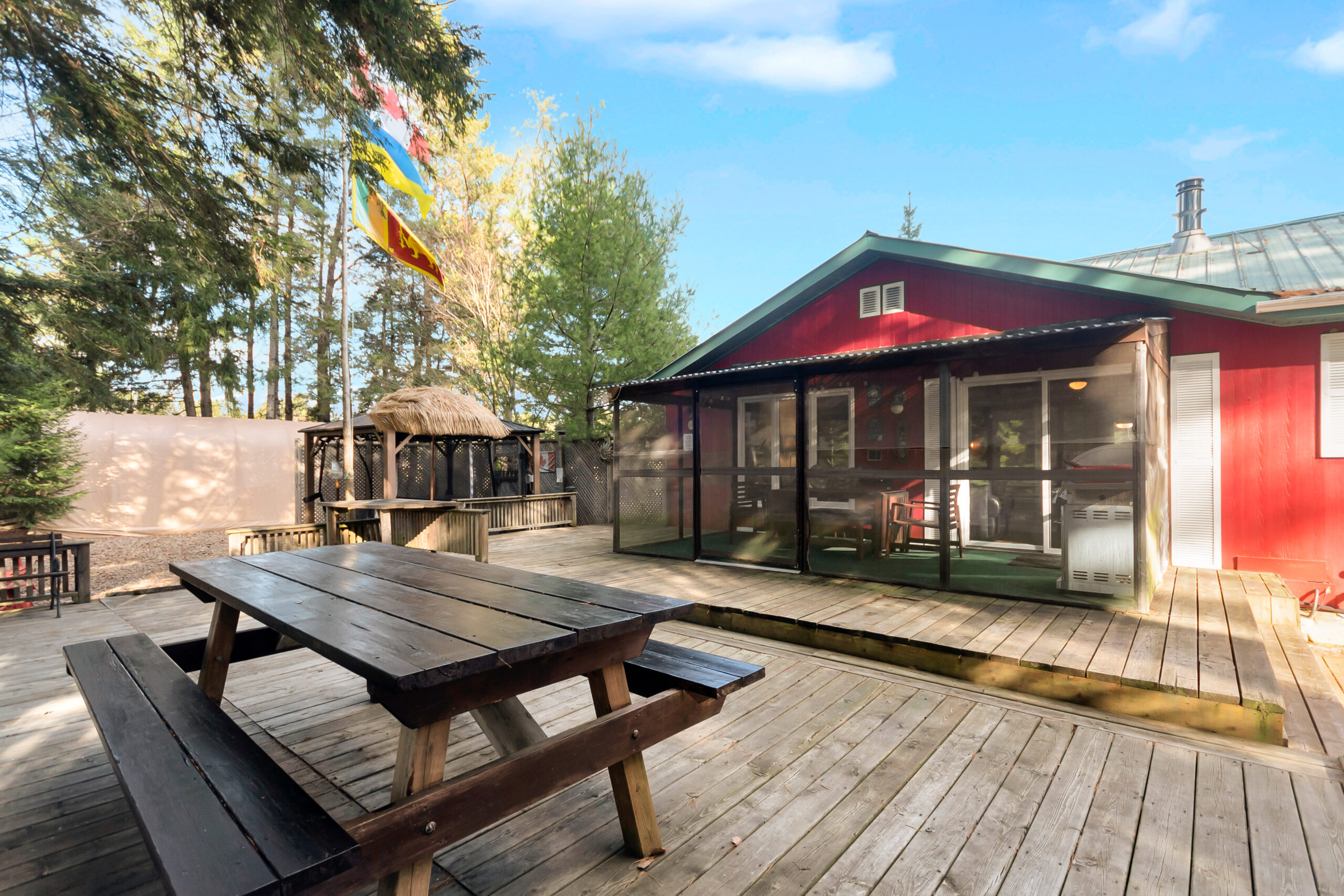 A wood picnic table on a wood deck next to a red cottage