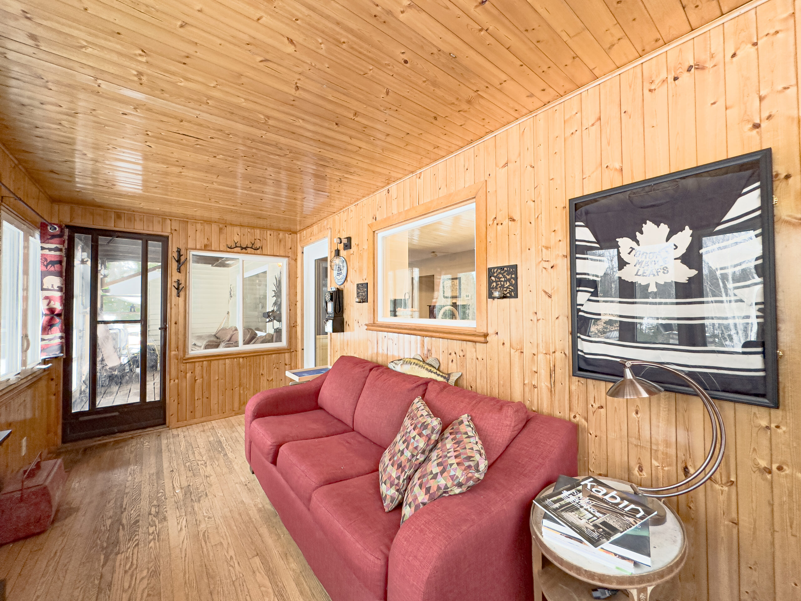 A red couch in a wood sunroom faces out to the windows