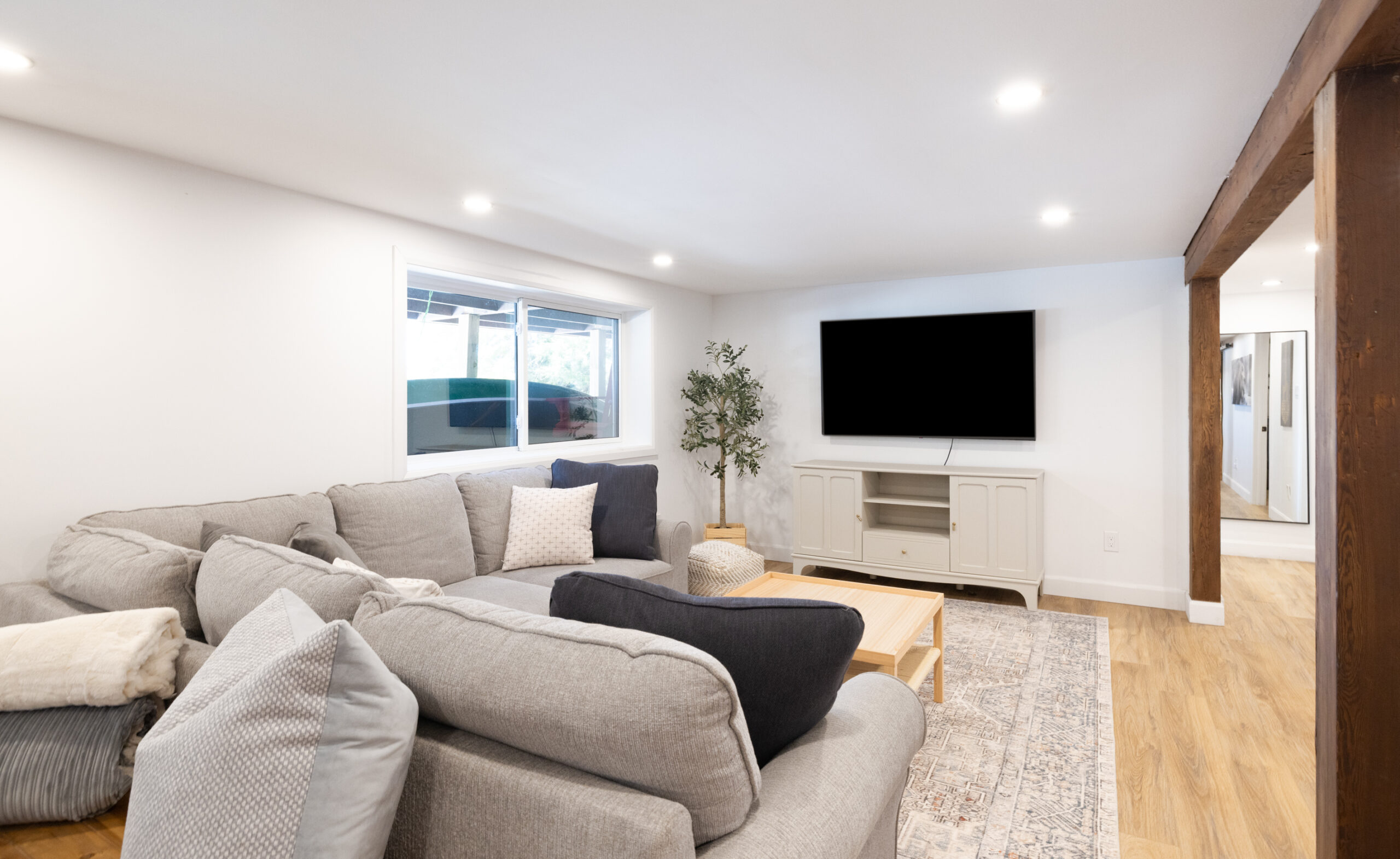 A grey couch faces a wall-mounted TV in a white basement