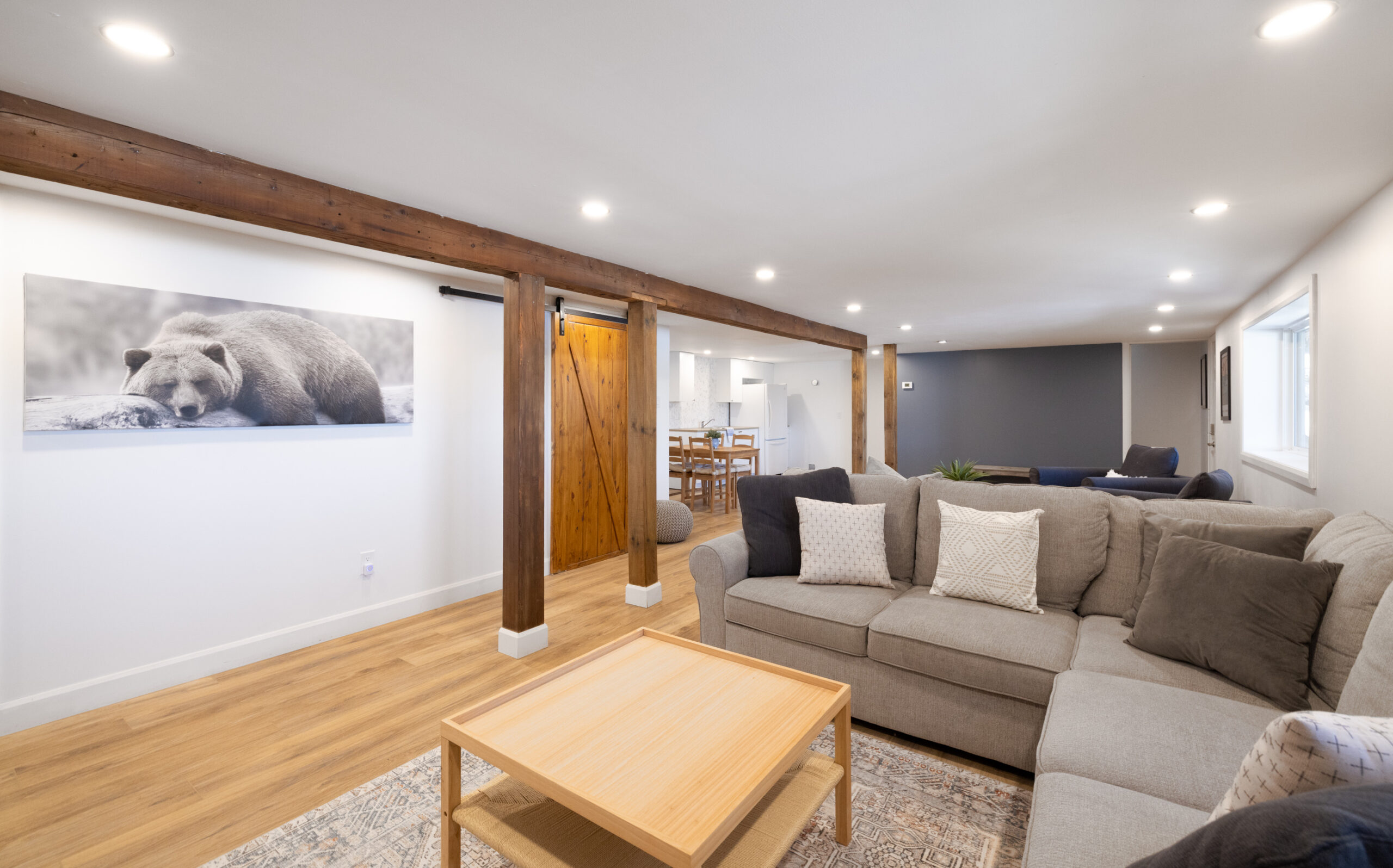 A grey L-shaped couch faces a wood coffee table in a white and grey basement
