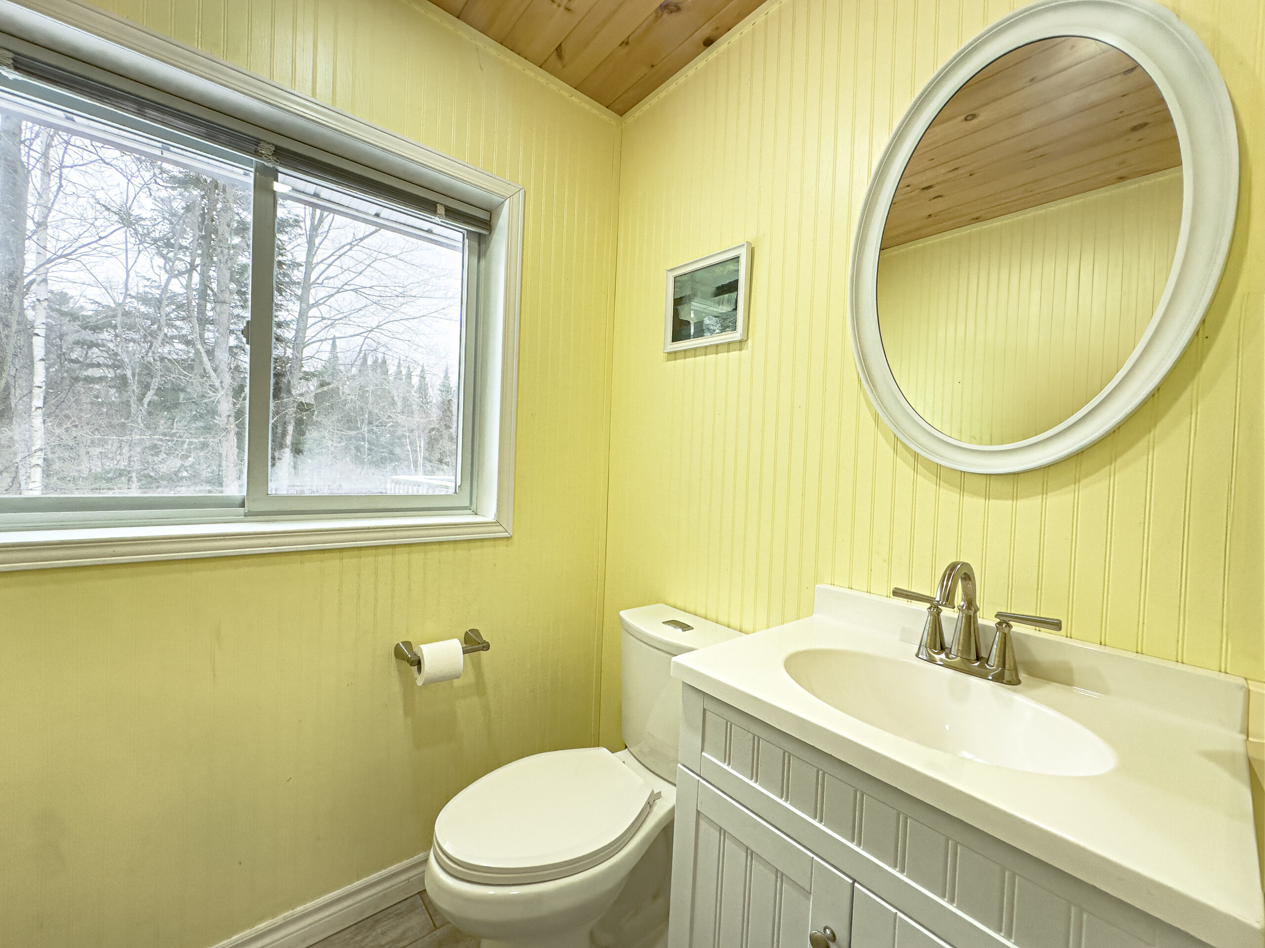 A white vanity with a round mirror in a light yellow bathroom