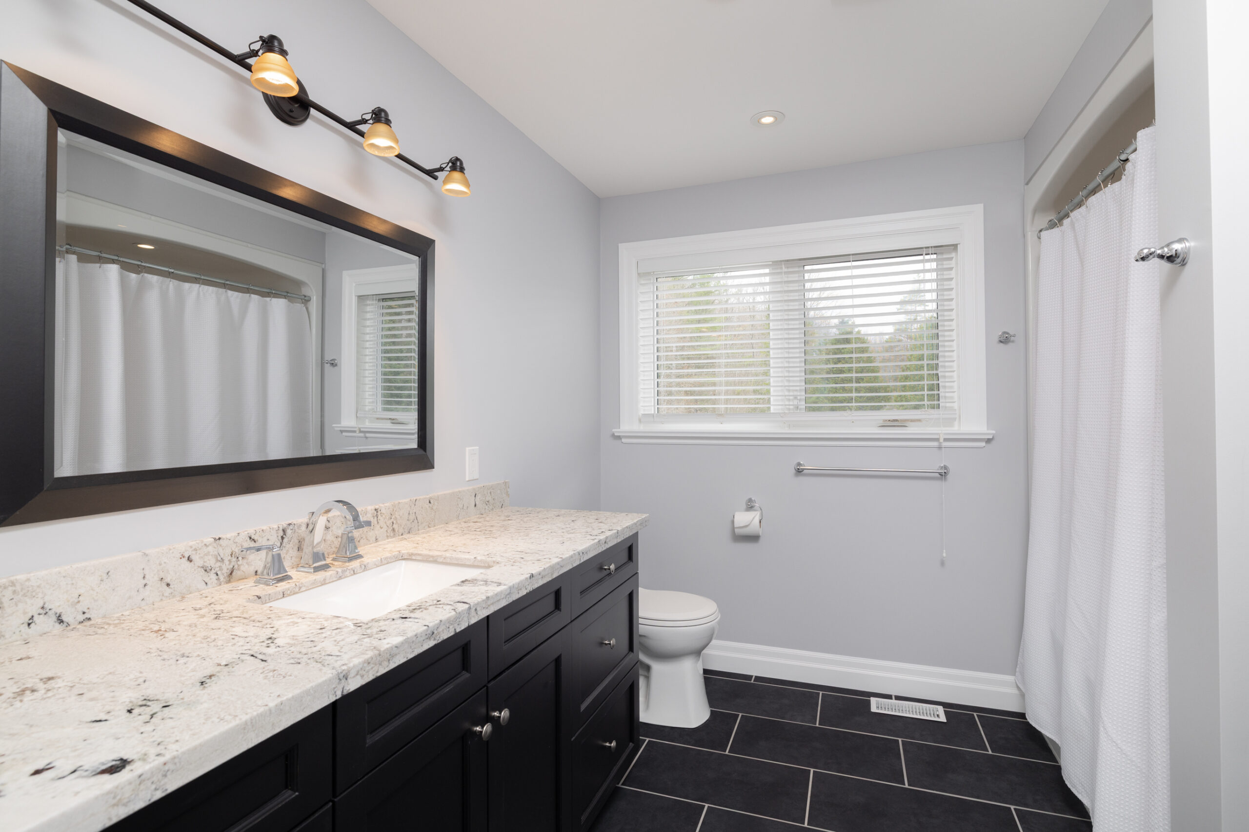 Bathrrom with a vanity and sink, toilet, window, and mirror.