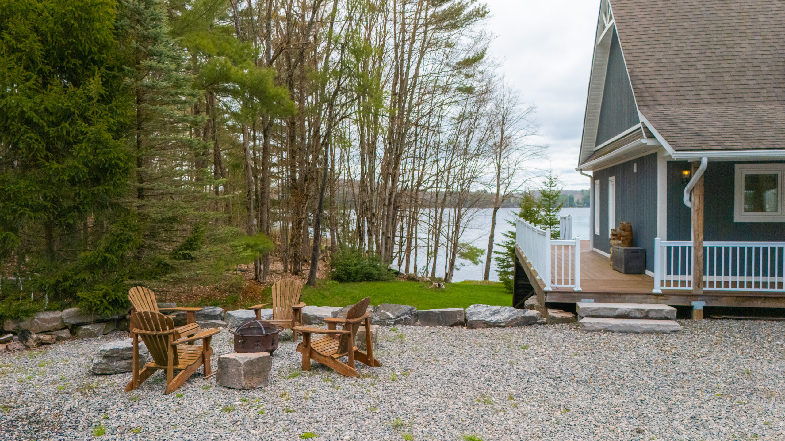 Fire pit surrounded by muskoka chairs with a lake in the background.