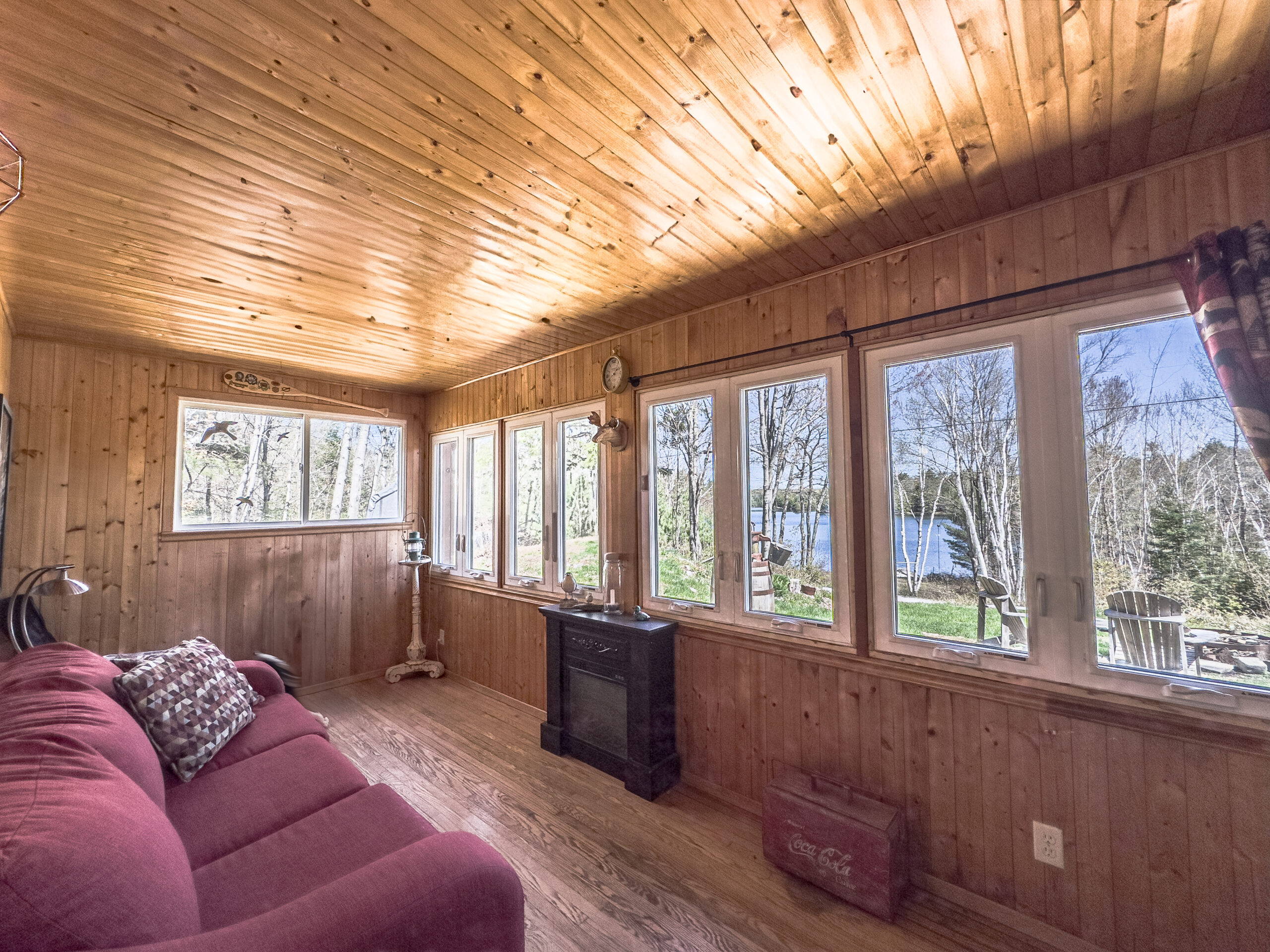 A wood-paneled sunroom with a red couch facing the windows