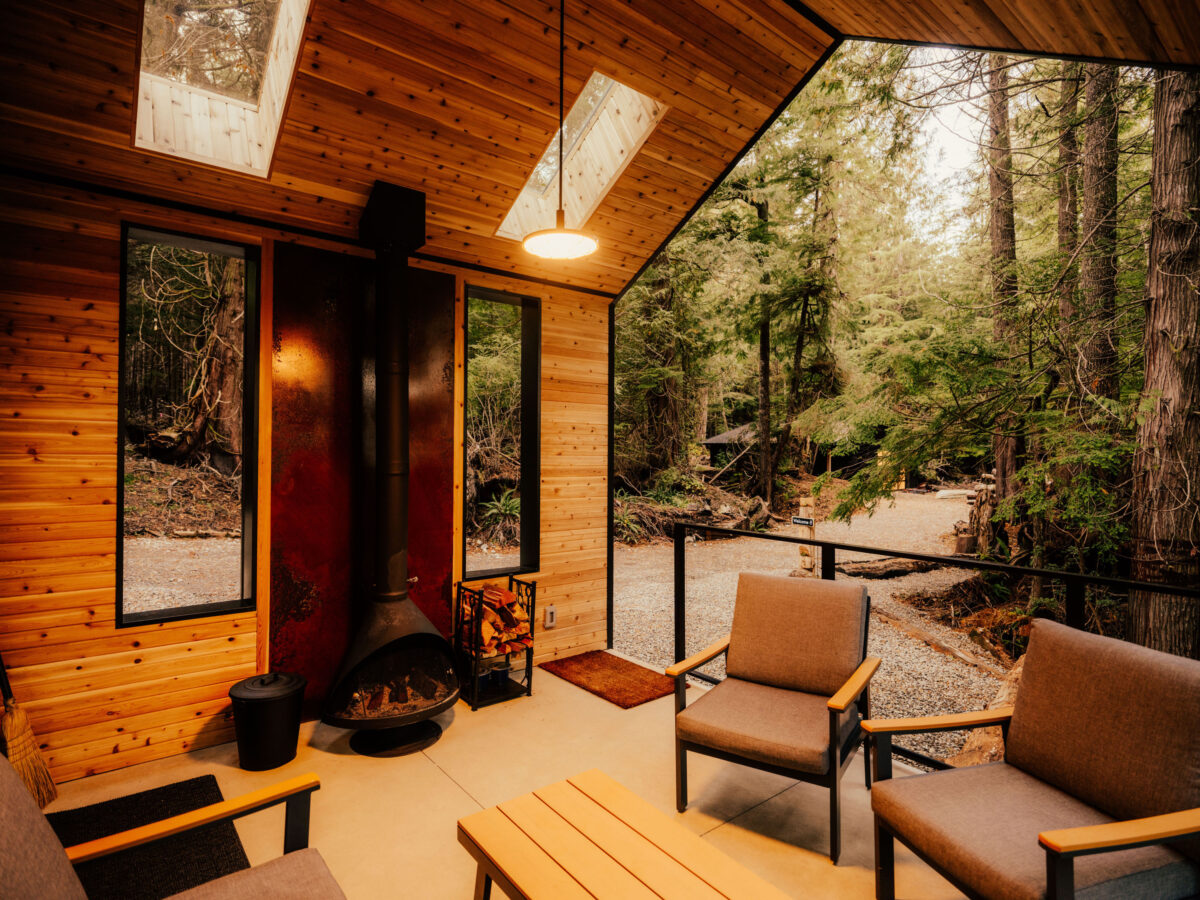 The inside of a modern wood cabin and the wall behind the fireplace is covered in sheet metal