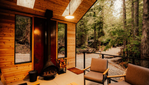 The inside of a modern wood cabin and the wall behind the fireplace is covered in sheet metal