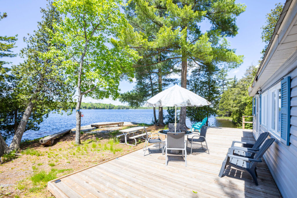Sunny wooden deck with seating and umbrella table, surrounded by trees and water views