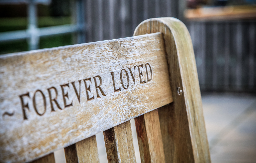 A wooden memorial bench with an "Forever Loved" engraved in it.