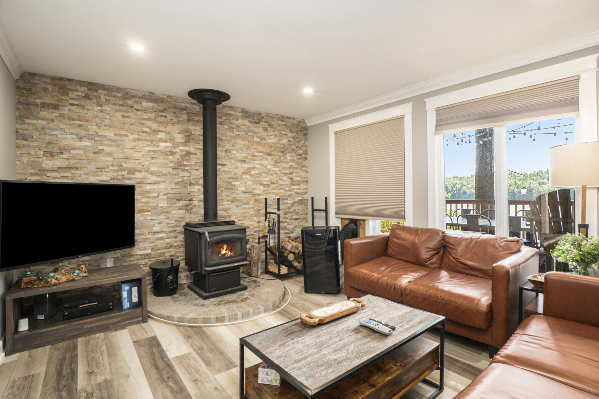 Inviting living room with wood-burning stove, stone feature wall, and large windows overlooking the property