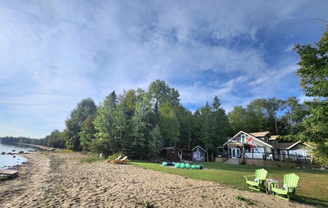 Sandy beach shoreline of 76 Serendipity Lane with view of the house and treed lot