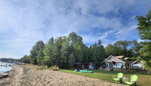 Sandy beach shoreline of 76 Serendipity Lane with view of the house and treed lot