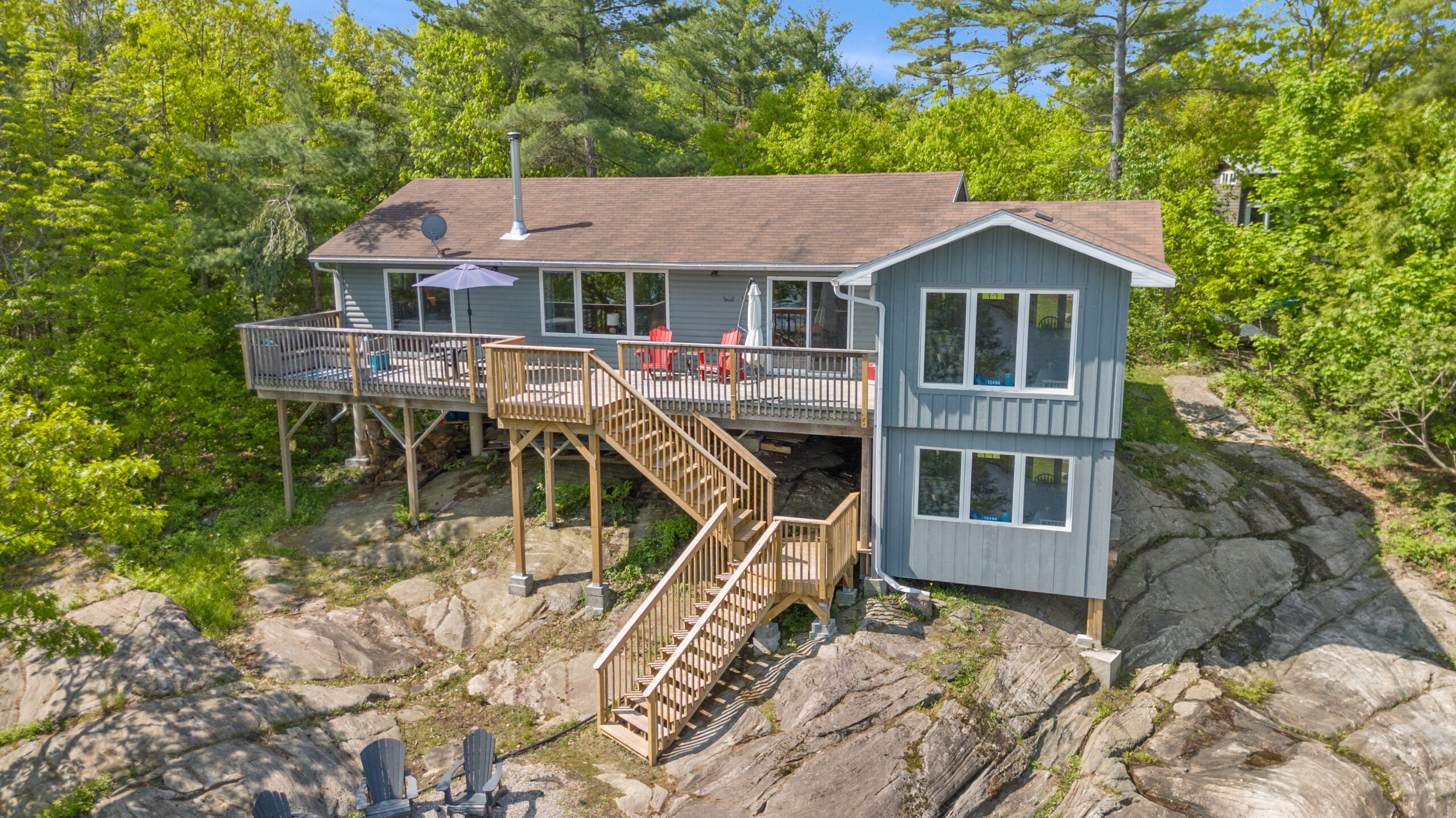 A multi-level grey cottage with wood stairs leading down to the lake