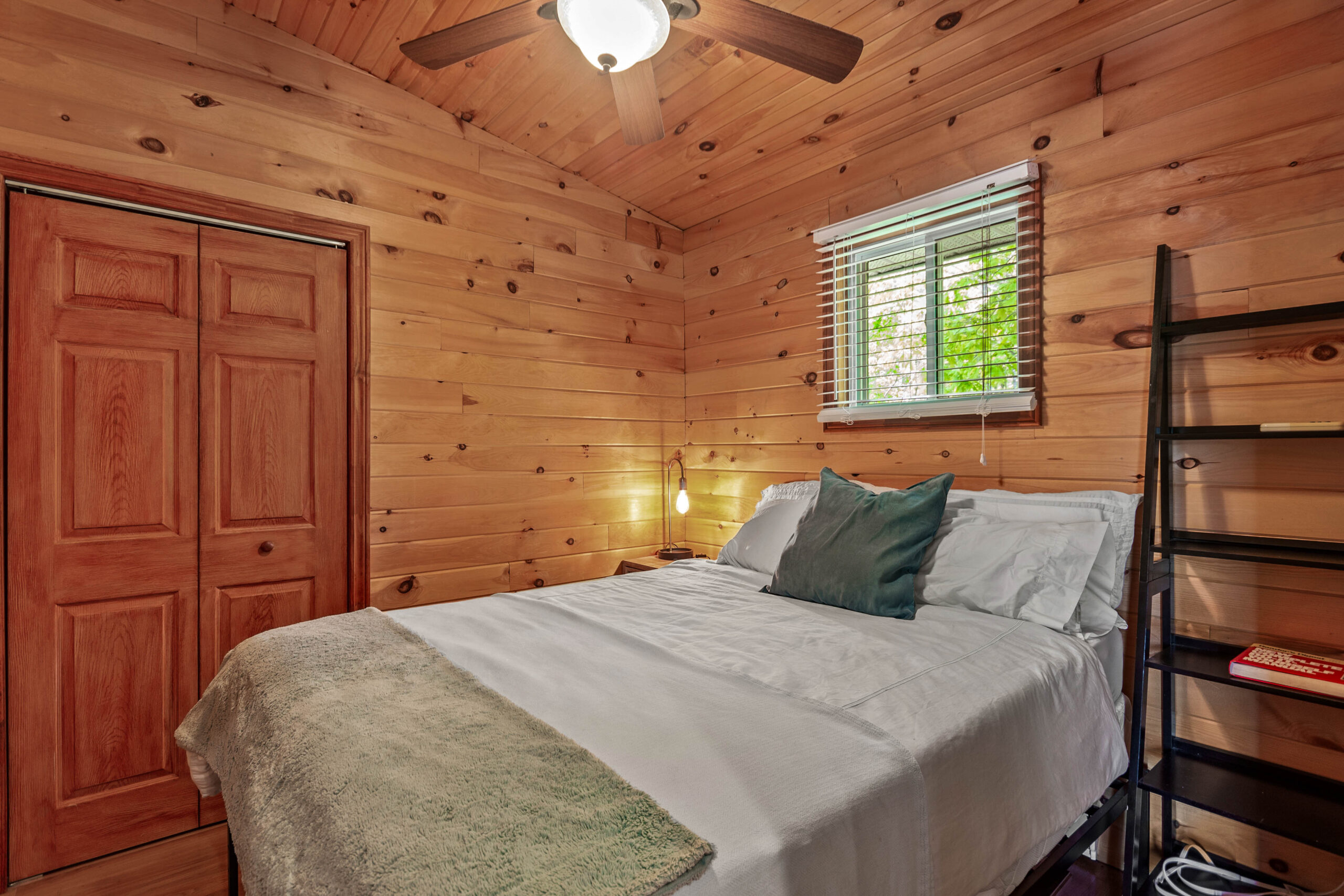 A white bed with a green throw blanket in a wood paneled room