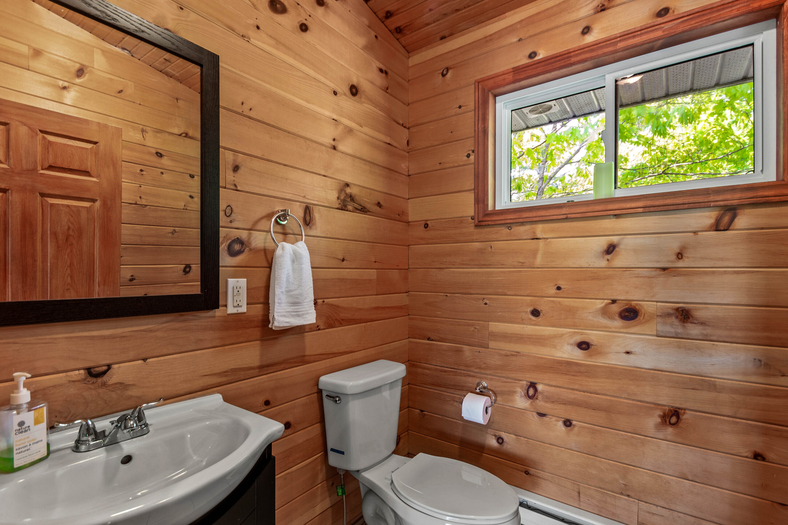 A wood paneled bathroom with a white vanity and square mirror