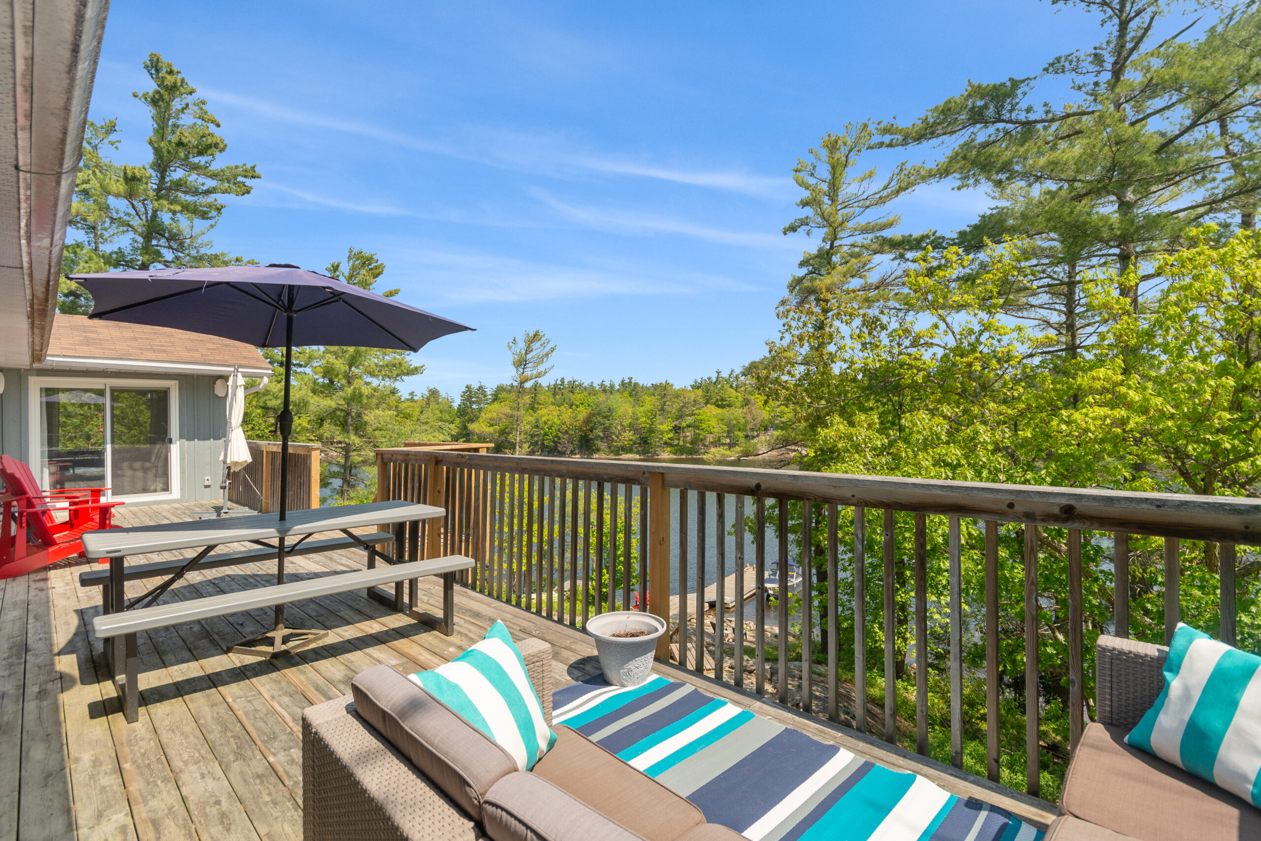 A grey couch with a blue striped carpet on a deck faces out into the forest