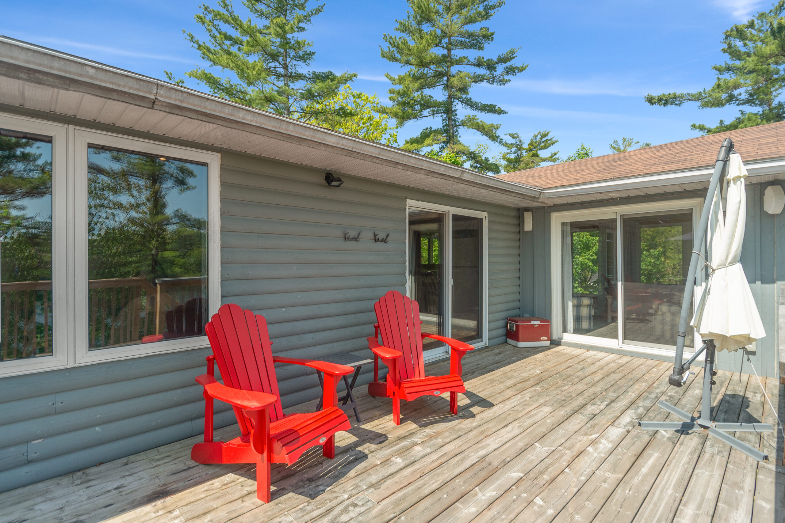 Two red Muskoka chairs outside a grey cottage on a deck