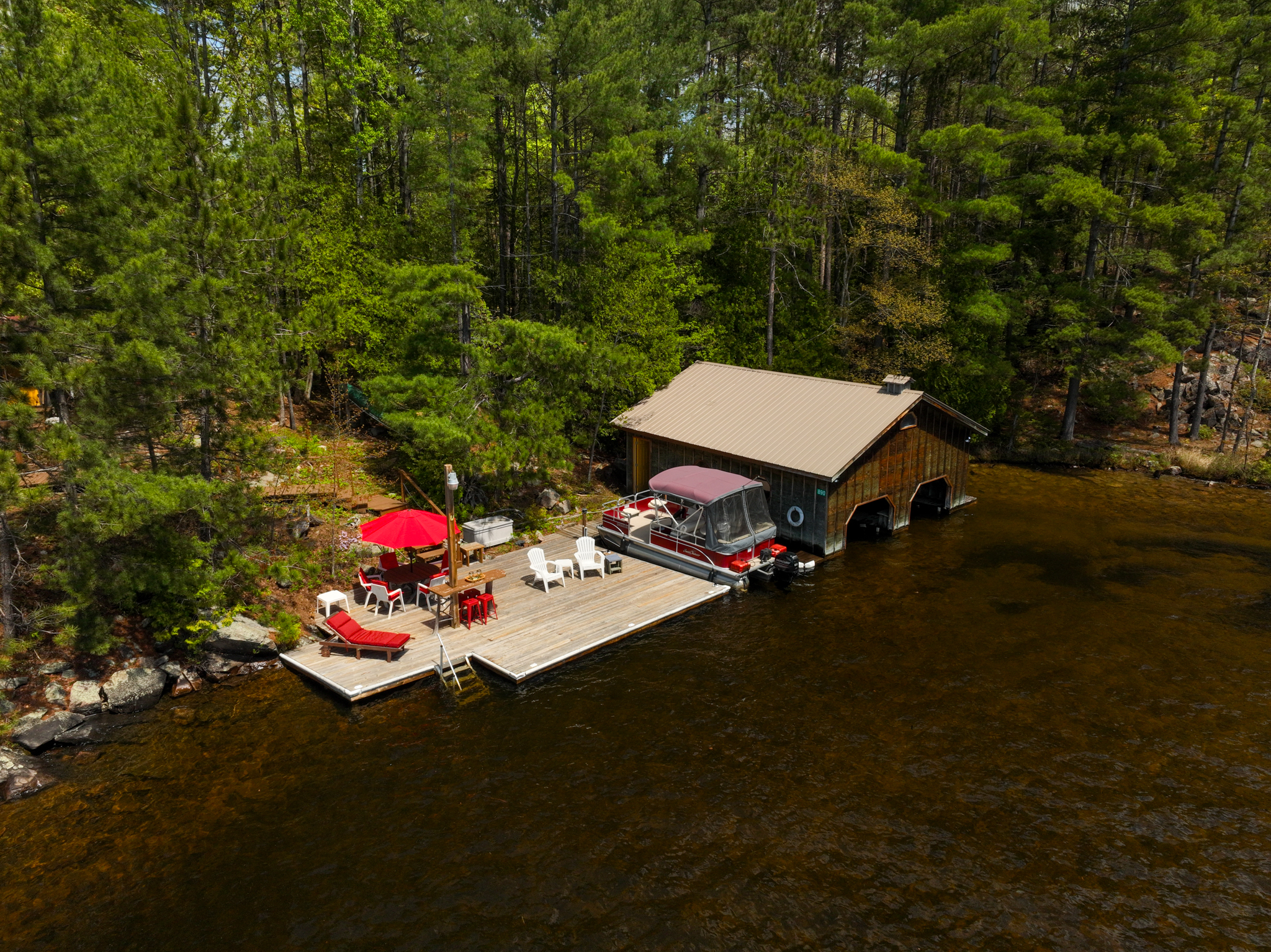 Elevated view of boathouse with boats and dock surrounded by forested shoreline