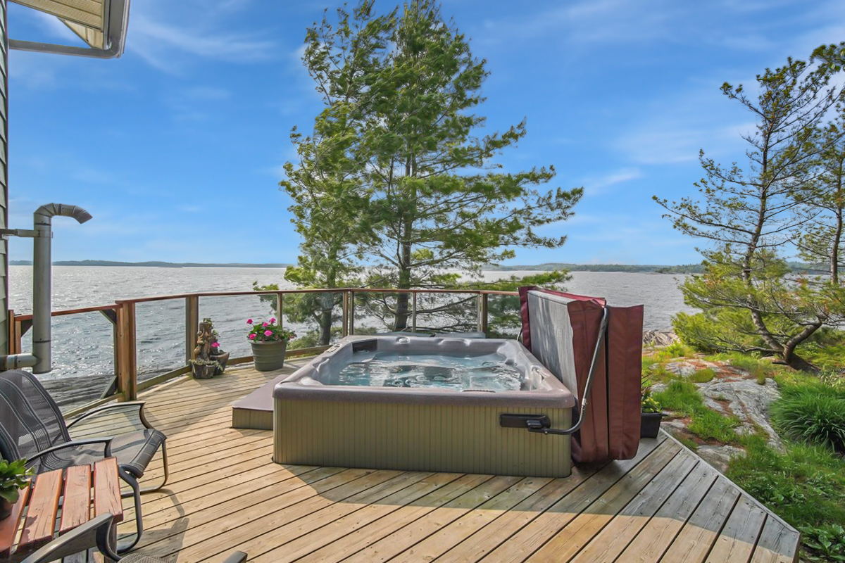Private outdoor hot tub on a wood deck with scenic views of the water and pine trees
