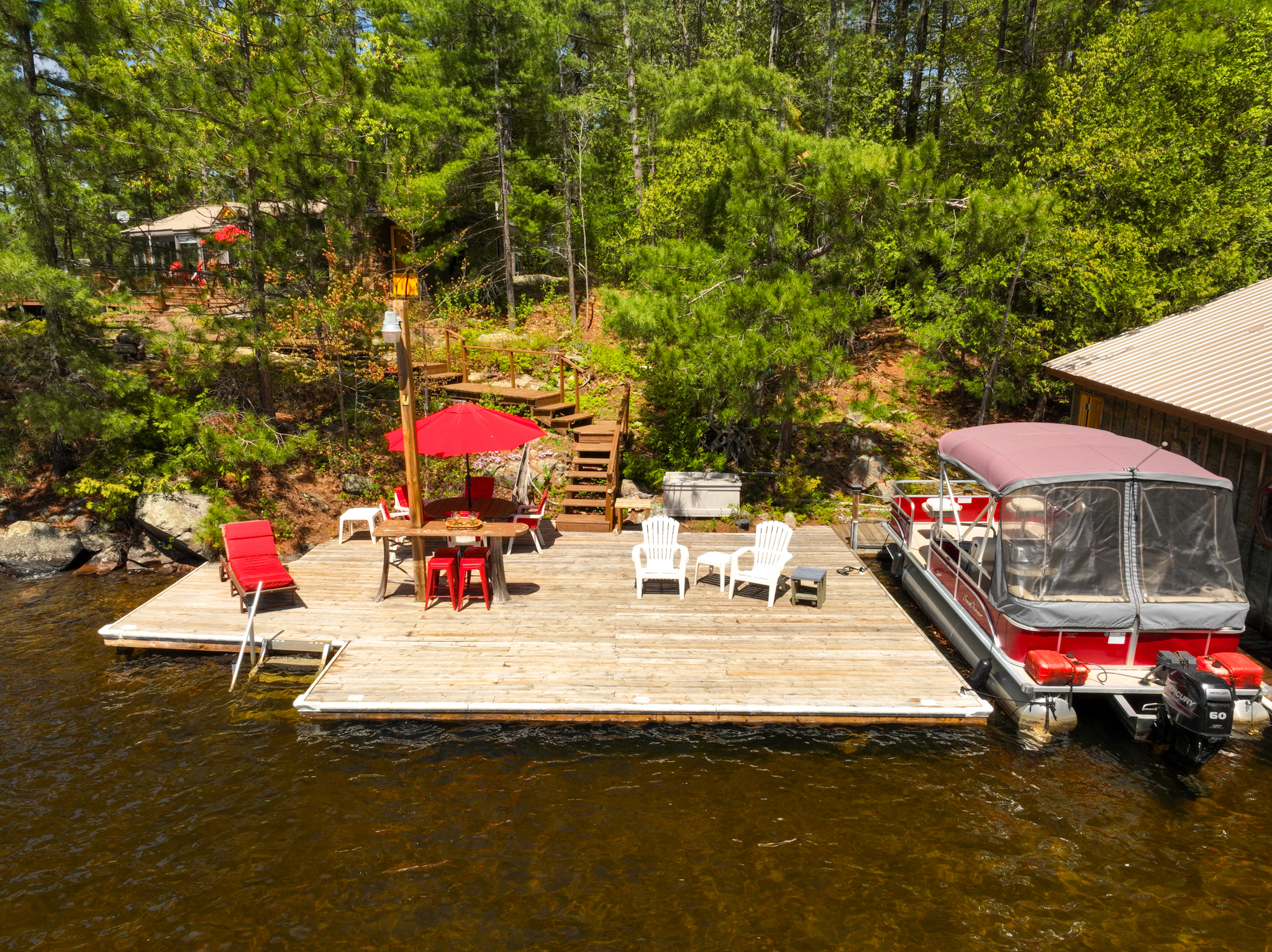 Lakeside floating dock with red umbrella, lounge chairs, and a boat tied up along the shore of Mazinaw Lake