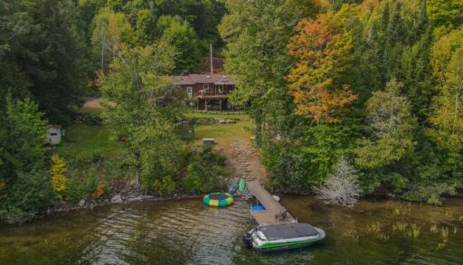 Drone shot of the cottage's private dock and gentle lakefront entry, with surrounding forest.
