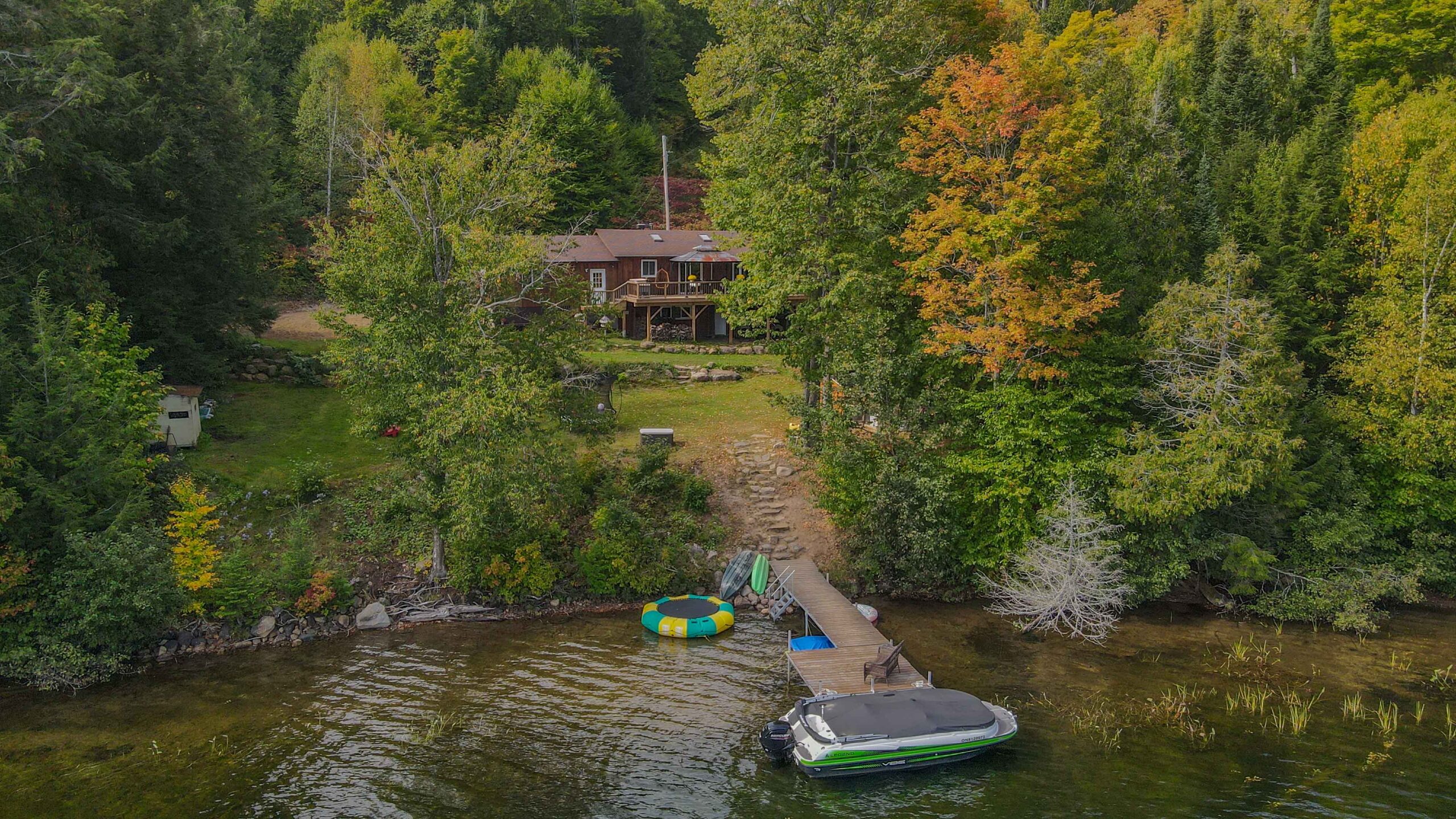 Drone shot of the cottage's private dock and gentle lakefront entry, with surrounding forest.