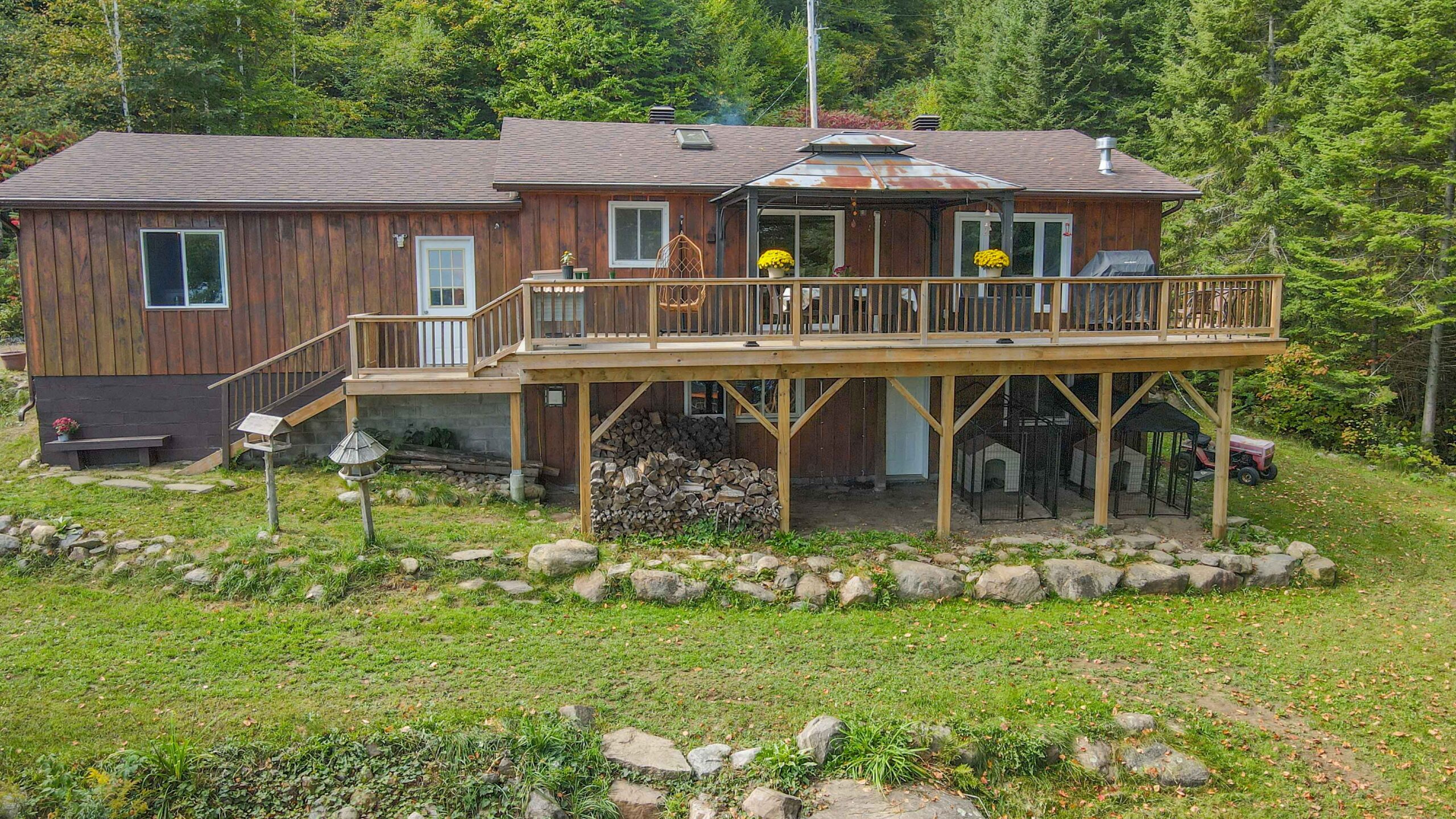 Ground-level view of the back of the cottage with a large wooden deck and stone landscaping.