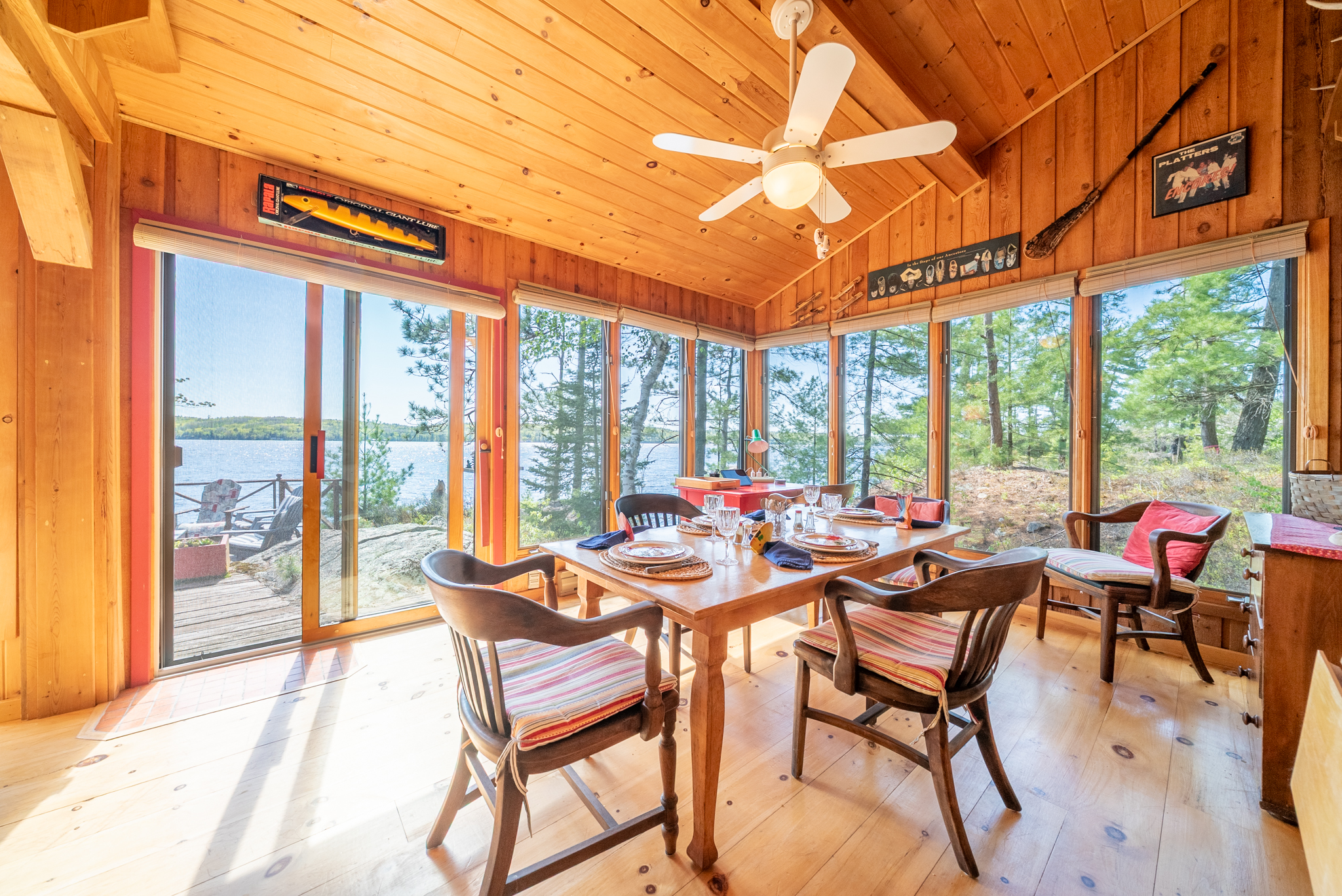 Bright dining space surrounded by large windows overlooking Mazinaw Lake, featuring wood walls and natural light