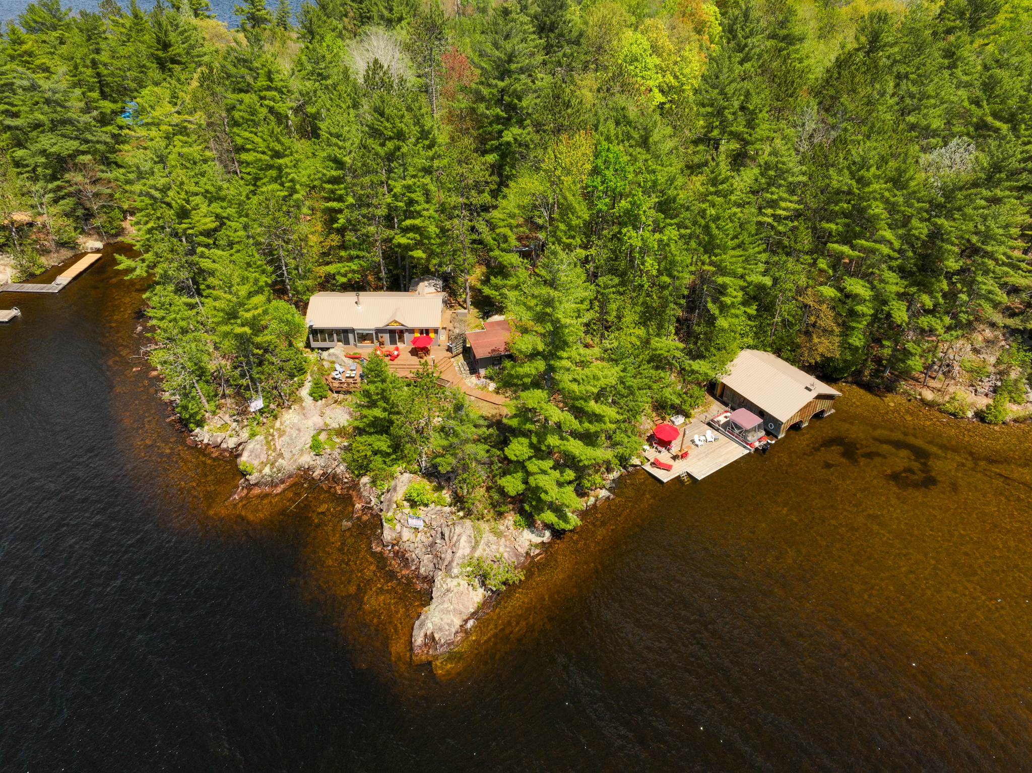 Drone shot capturing the shoreline, dense forest, sandy beach, and boathouse of 890 Mazinaw Lake