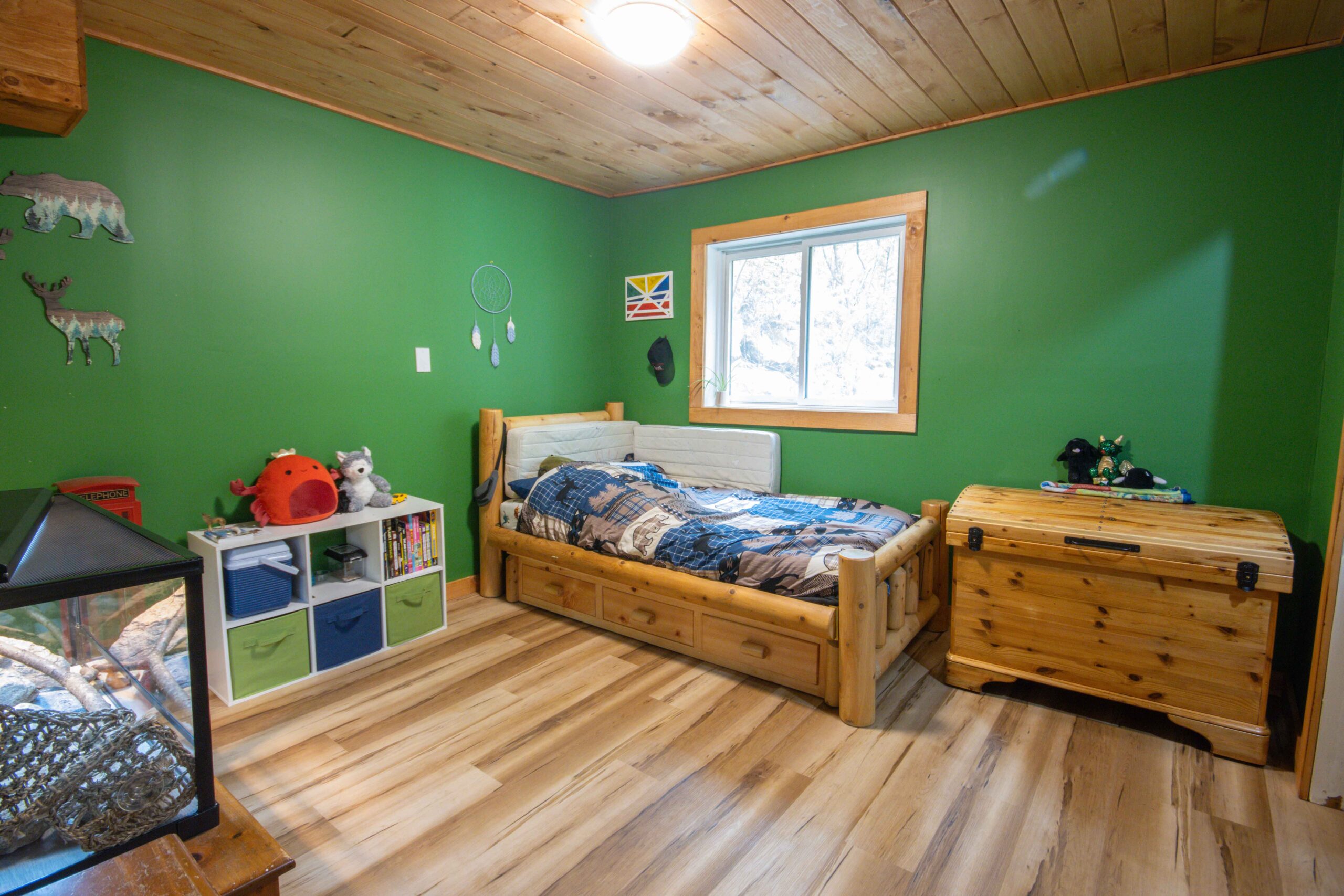 Playful children’s room with green walls, toy bins, and a rustic bedframe.