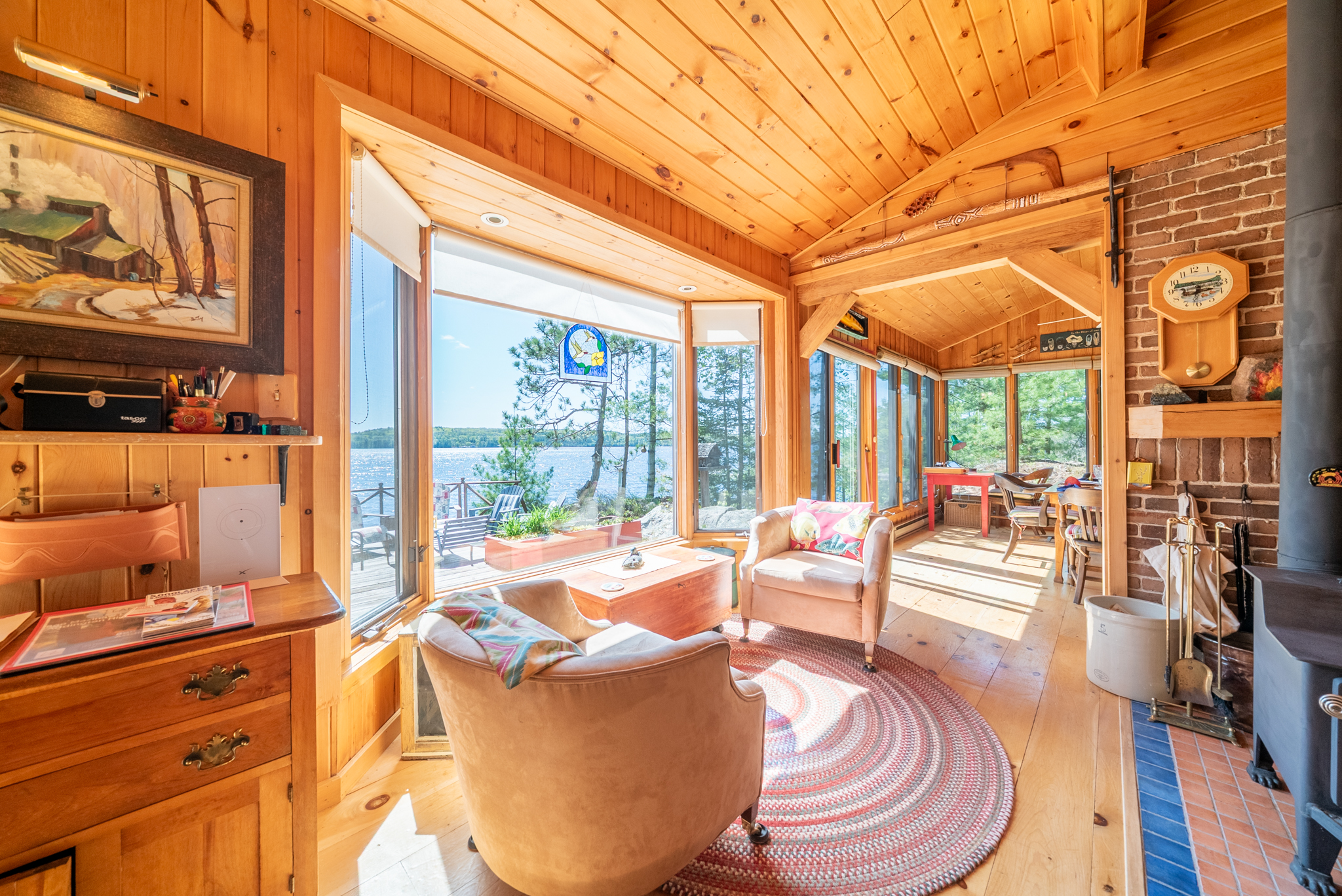 Warm wood-paneled living space with armchairs, picture windows, and lake views from inside the cottage