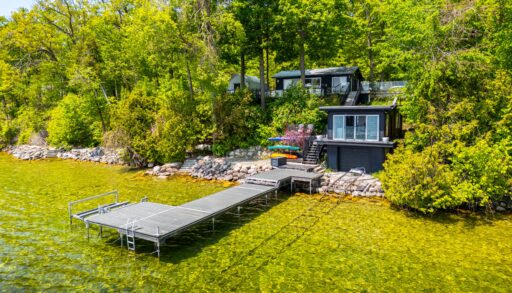 A black paneled cottage with a long deck that juts out into green-blue water