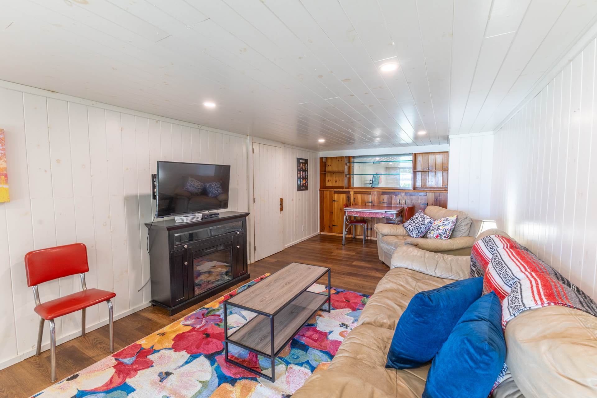 A light brown couch facing a fireplace and TV mounted on the wall with a colourful carpet