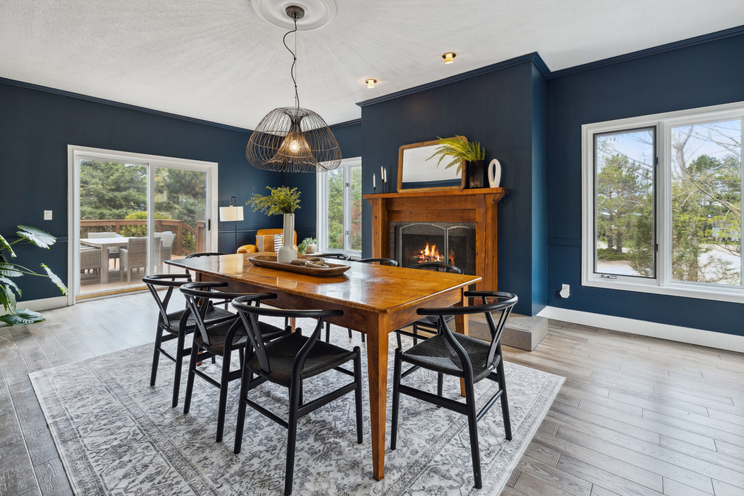 A wood dining table with black chairs in a dark blue room with windows