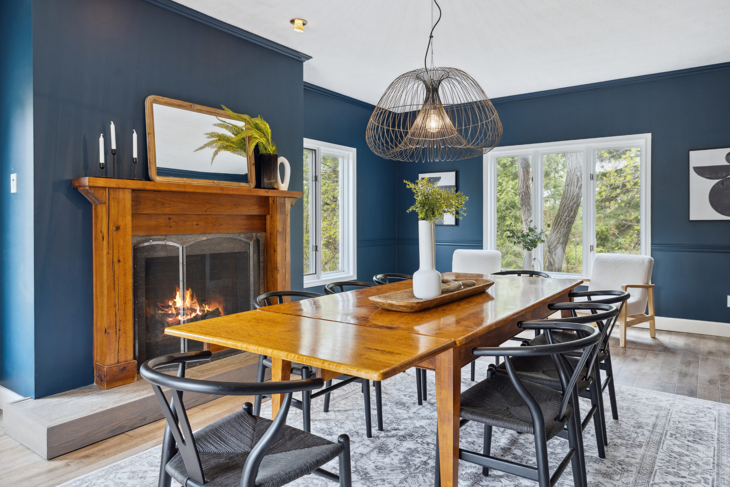 A wood dining table with black chairs in a dark blue room with windows