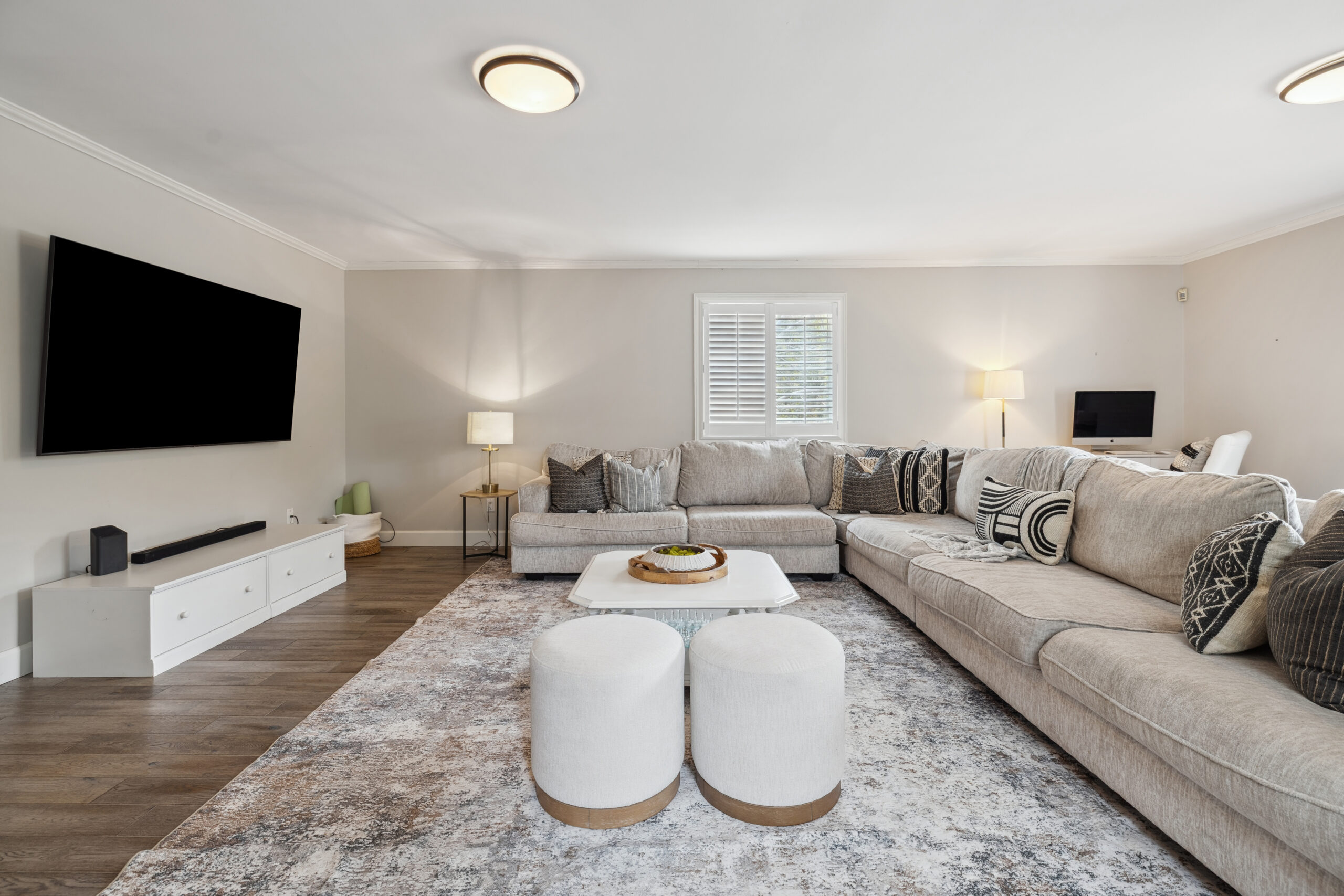An L-shaped couch on a patterned carpet faces a TV mounted on a white wall
