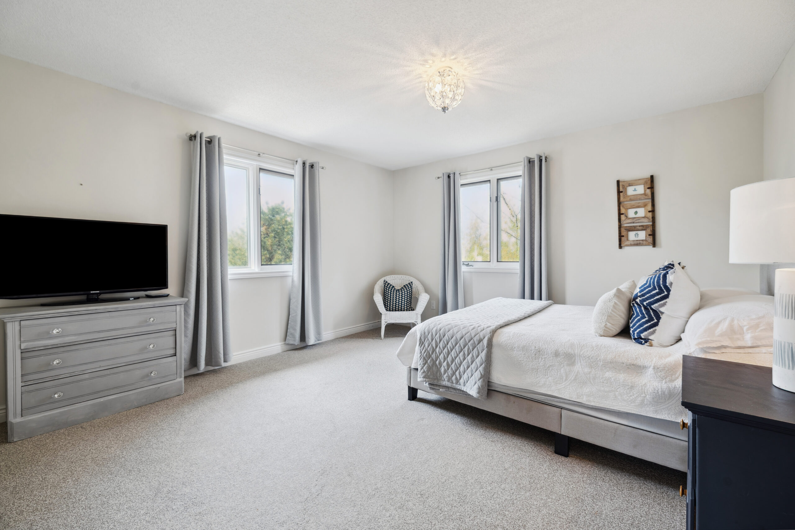 A white bed with blue pillows in a white room with bright windows