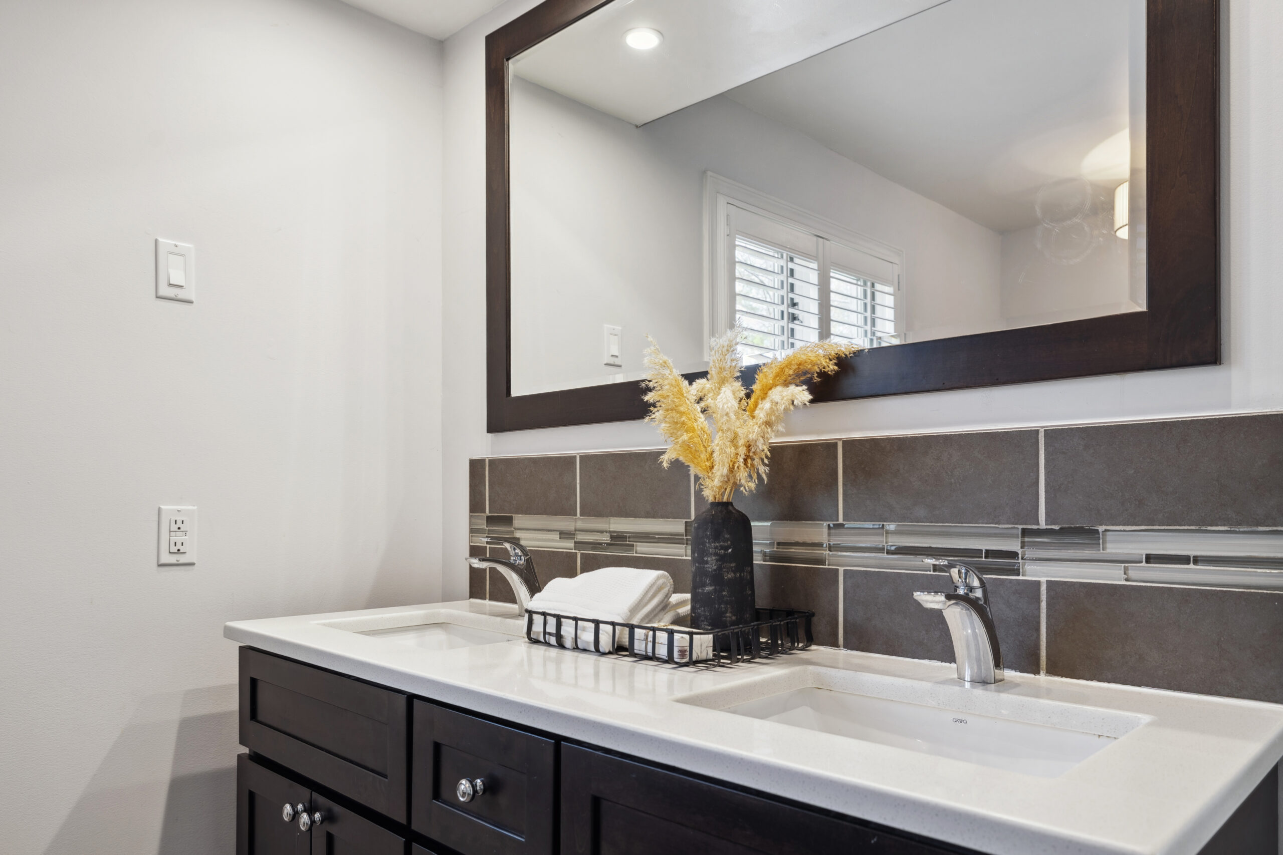 A bathroom with a dark wood vanity and large mirror