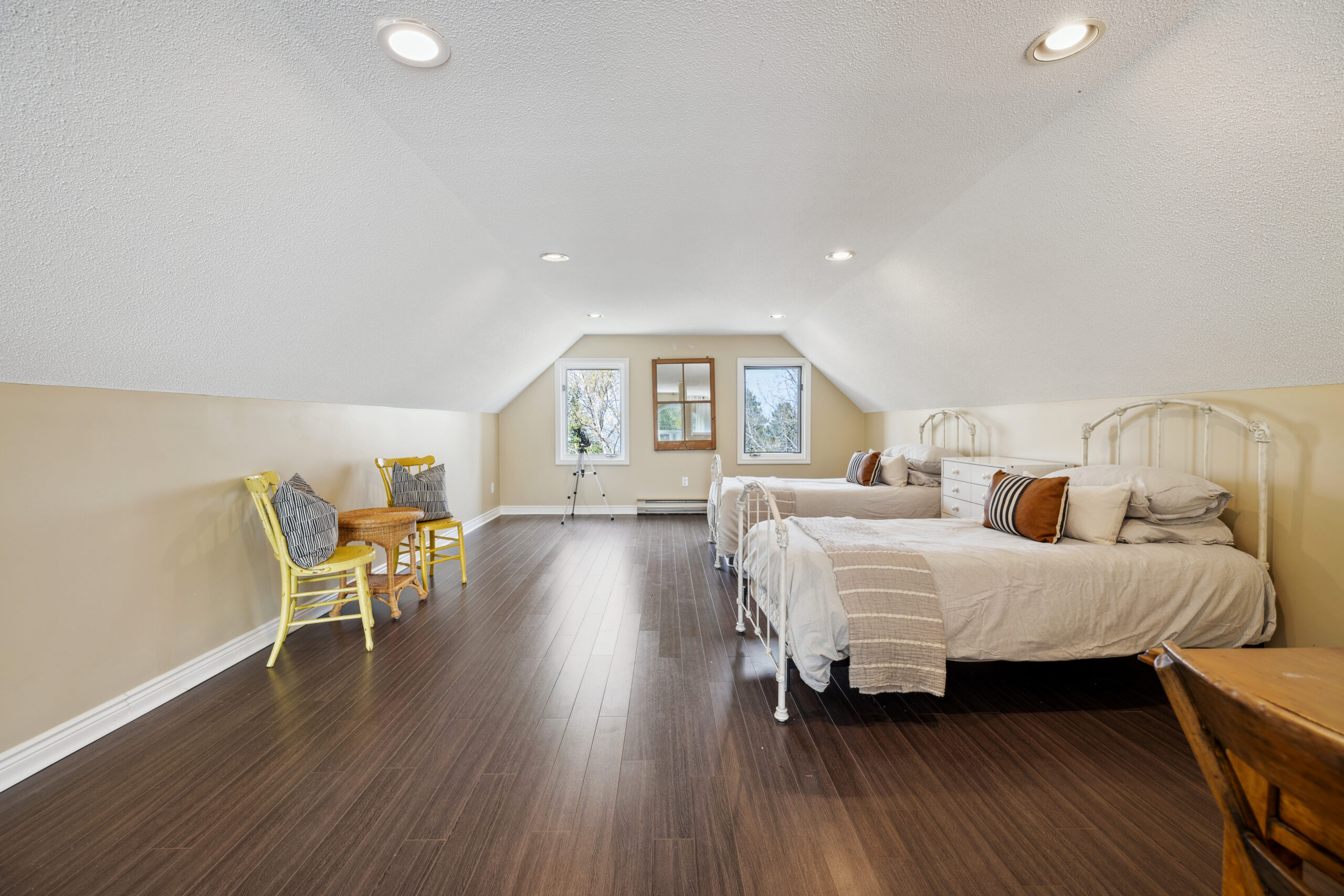 Two twin beds face two yellow chairs in a loft