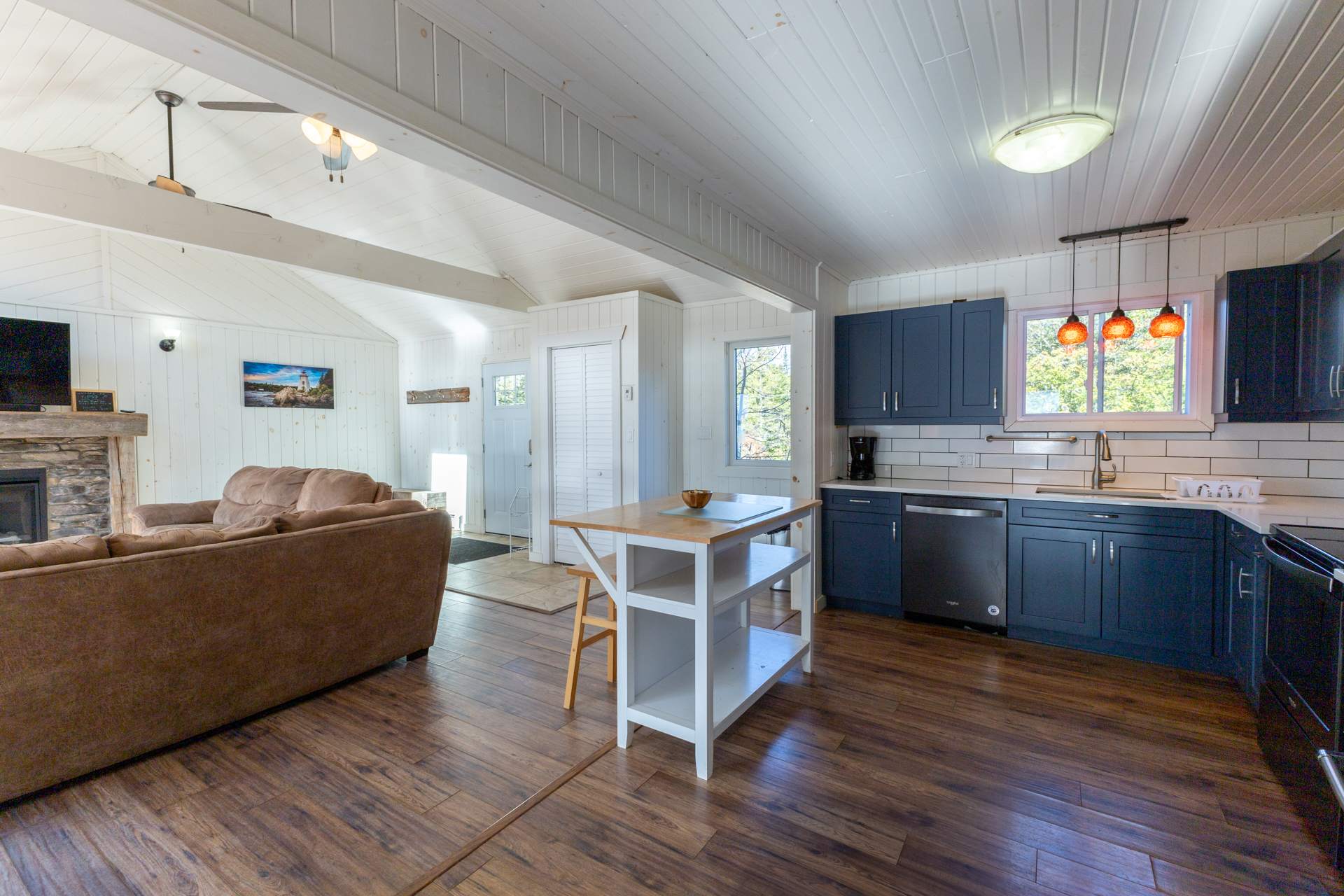 An open-concept living area. To the left, a brown couch. To the right, a blue kitchen with a white island